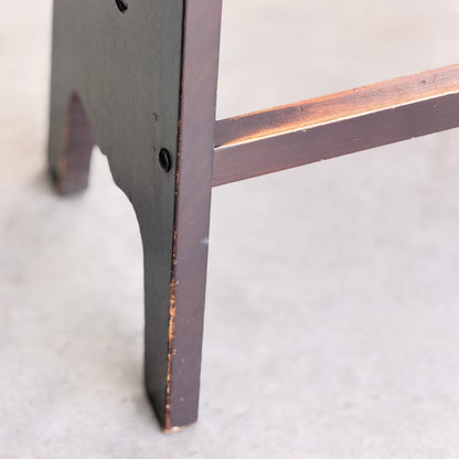 Close-up of the leg and support bar of a 1970s Australian Mid-Century Modern Spanish Revival Davis Stool from the Revive set of 3, showing visible wear on the dark wood finish, set against a light-colored floor.