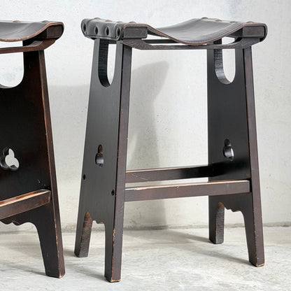 A close-up of the 1970s Australian Mid-Century Modern Spanish Revival Davis Stools – Set of 3 (Revive), showing curved seats and leg cutouts, set on a light concrete floor against a textured white wall.