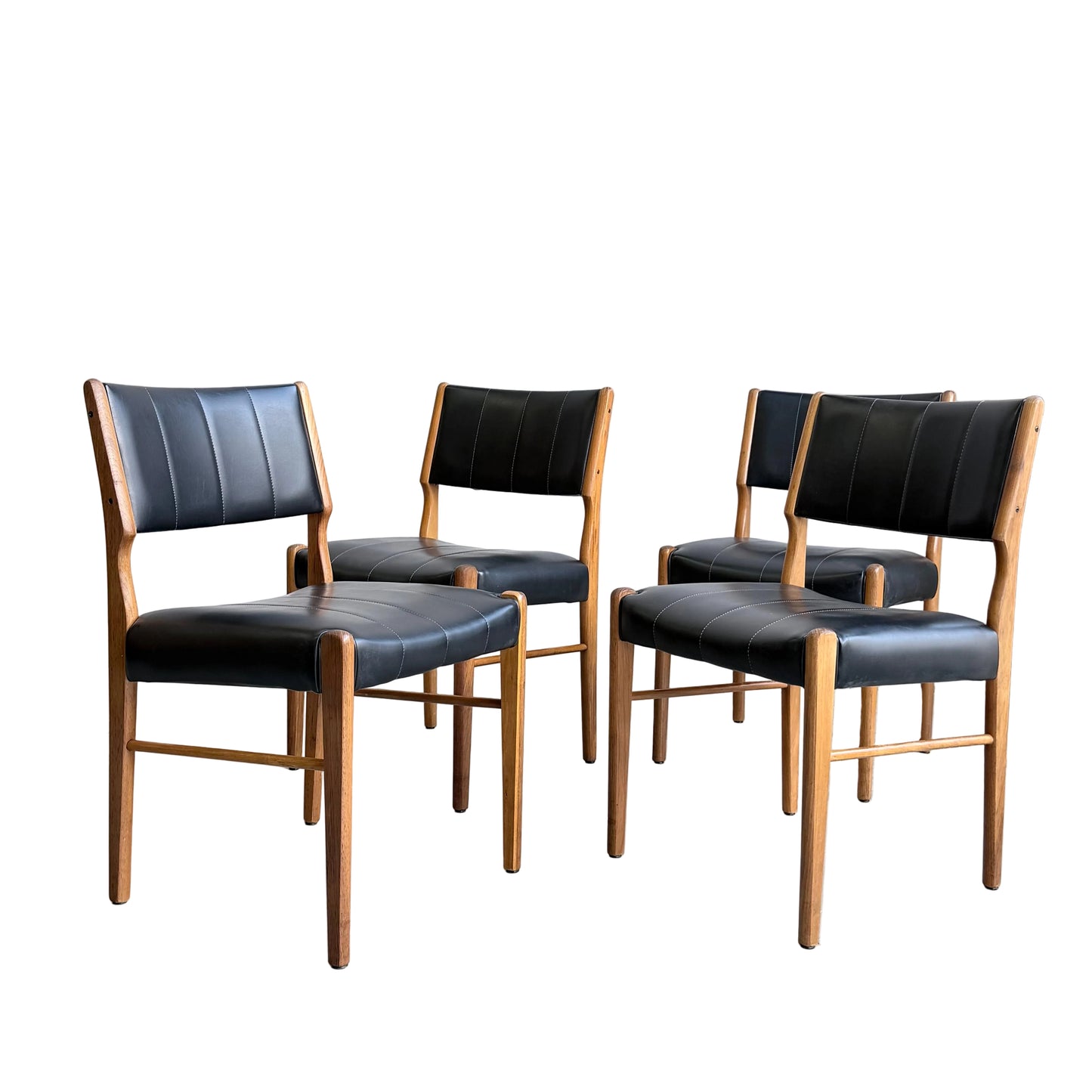 A set of four Vintage TH Brown Blackwood Dining Chairs (Revive) with black cushioned seats and backs, showcasing a refined mid-century modern design, are arranged in a spacious room with light gray concrete walls and floor.