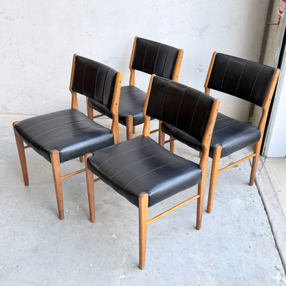 A set of four Vintage TH Brown Blackwood Dining Chairs (Revive), with black upholstered seats and backs and Tasmanian Blackwood frames and legs, are arranged on a concrete floor against a light gray wall.