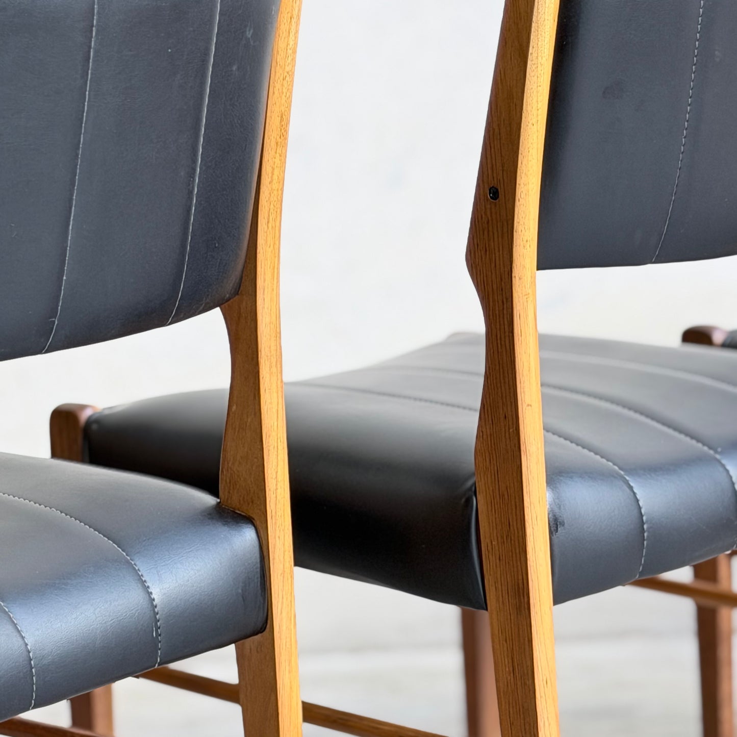 Two Vintage TH Brown Blackwood Dining Chairs from the Revive set of 4 feature black leather seats and backs with vertical stitching and smooth wood frames, shown side by side against a light background.