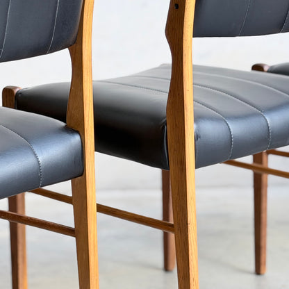 Close-up of two Vintage TH Brown Blackwood Dining Chairs – Set of 4 (Revive), with black leather seats and backs, visible stitching, and light brown wooden legs and frames on a light-colored floor.