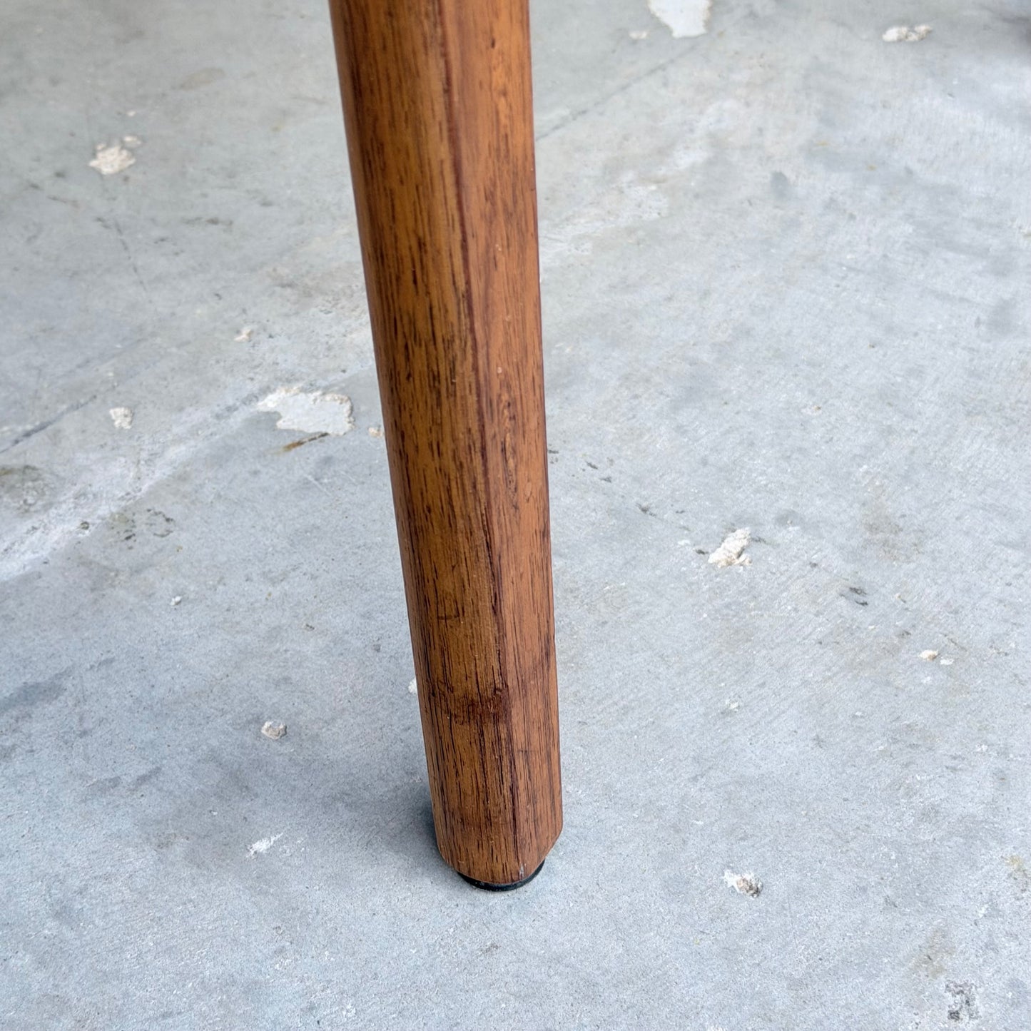 One leg of a Vintage TH Brown Blackwood Dining Chair from the Revive set of 4 stands on a light gray, slightly worn concrete floor.