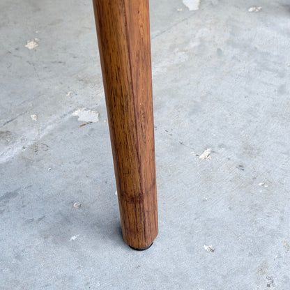 One leg of a Vintage TH Brown Blackwood Dining Chair from the Revive set of 4 stands on a light gray, slightly worn concrete floor.