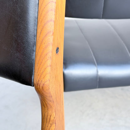 Close-up of a Vintage TH Brown Blackwood Dining Chair from the Revive set of 4, showcasing its wooden frame with a visible screw and black leather backrest and seat, placed on a light-colored floor.
