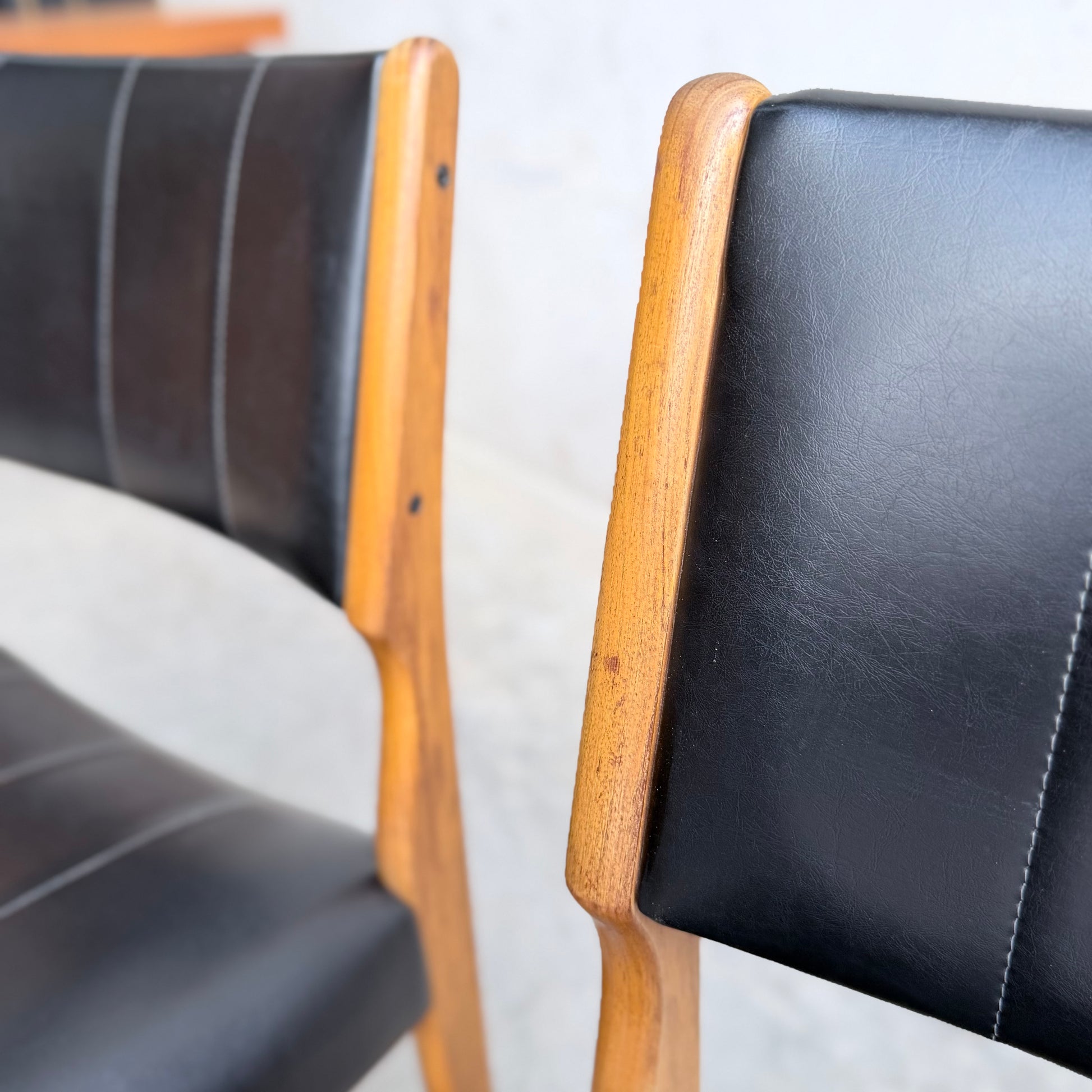 Two Vintage TH Brown Blackwood Dining Chairs (from a set of 4) with black leather seats and backs are shown side by side, focusing on the rich wood texture and fine leather upholstery of these elegant Revive dining chairs.