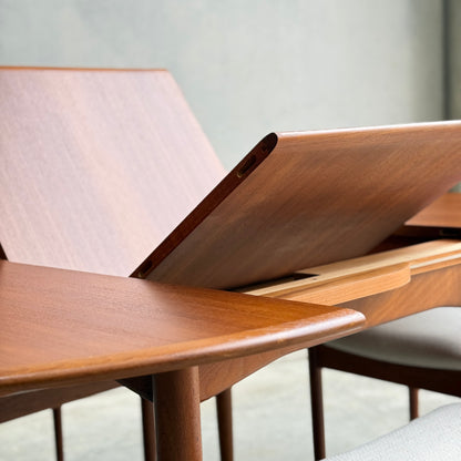 Close-up of a fully restored Parker 90 Round Extension Butterfly Table (Rediscover) with tilting surface, angled panels, smooth finishes, and clean lines. Light gray upholstered chairs appear in the background.