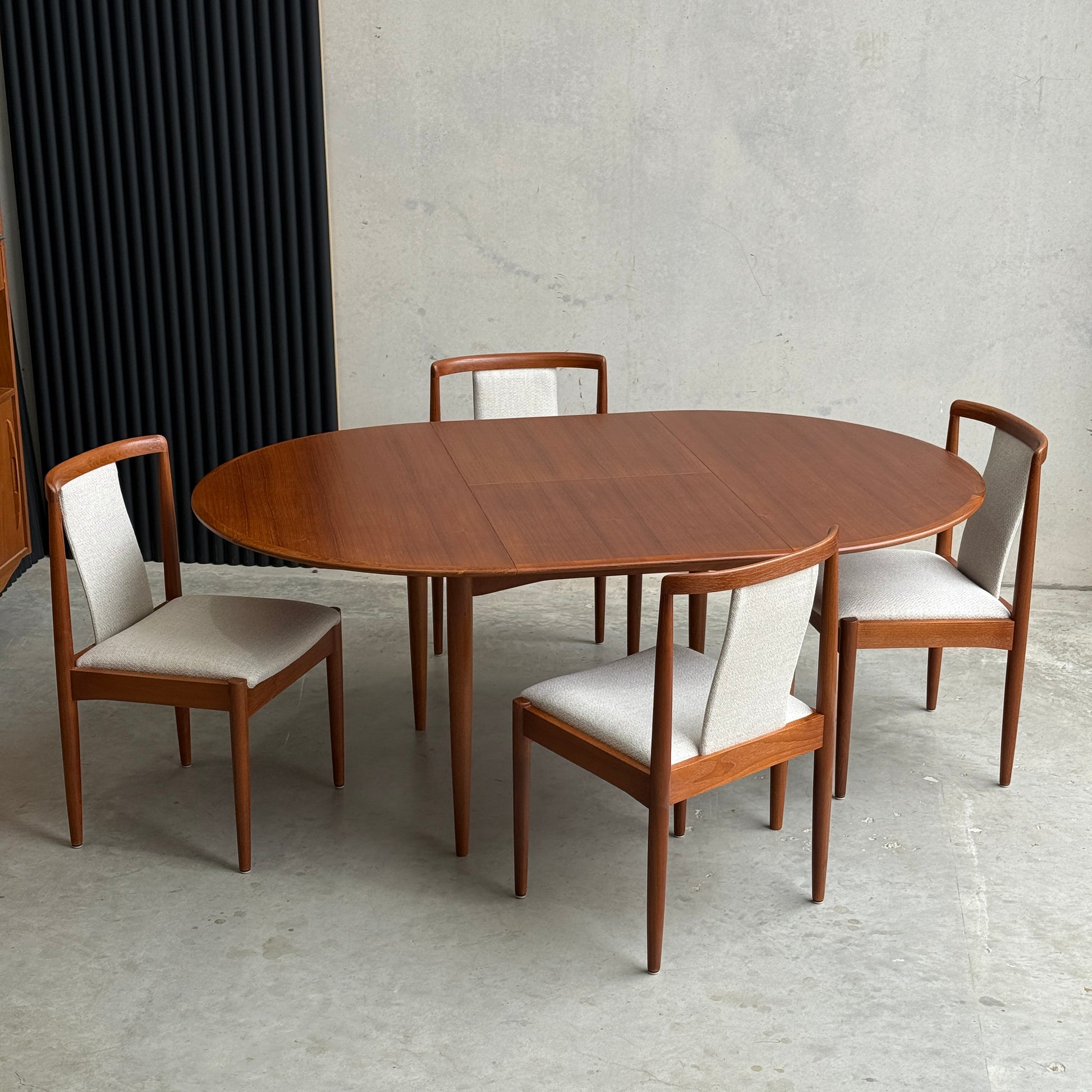 A minimalist room with concrete floors and walls features a fully restored Parker 90" round extension butterfly table (Rediscover), serving as the centerpiece in a mid-century modern dining setting.
