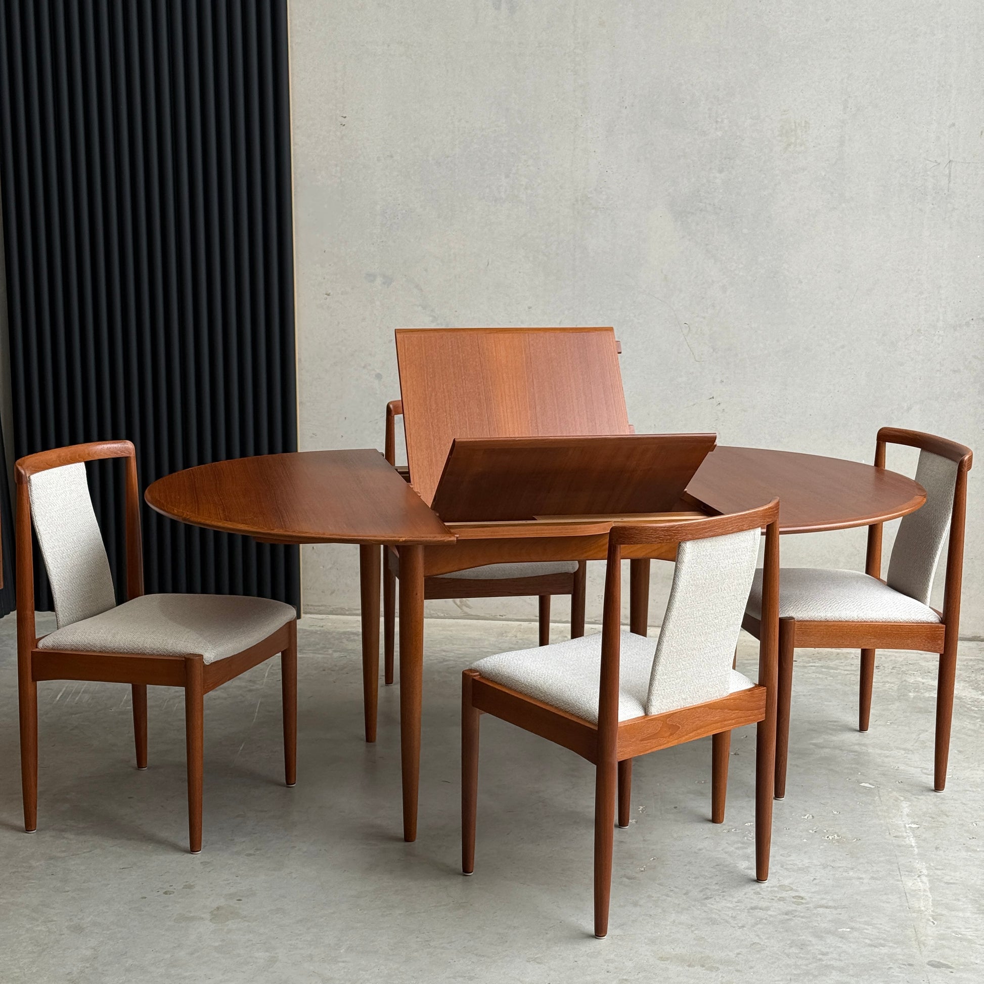 A Fully Restored Parker 90 Round Extension Butterfly Table Only (Rediscover) with its extension leaf partially raised sits against a minimalist concrete wall, making a true mid-century modern statement.
