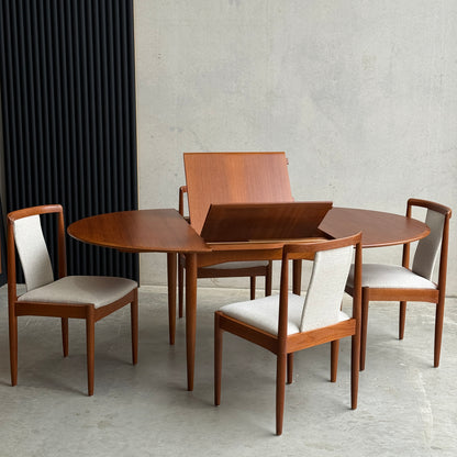 A Fully Restored Parker 90 Round Extension Butterfly Table Only (Rediscover) with its extension leaf partially raised sits against a minimalist concrete wall, making a true mid-century modern statement.