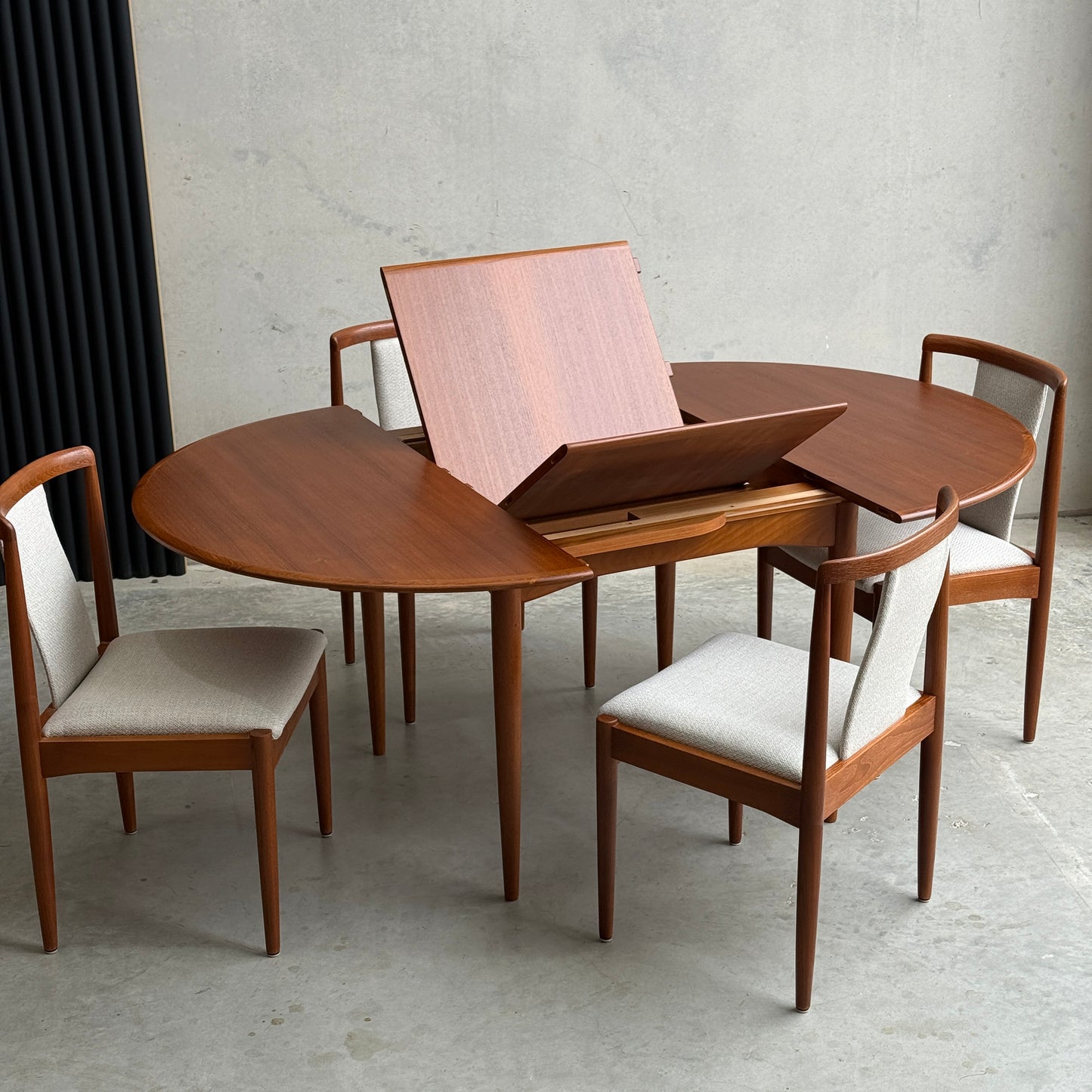 A fully restored Parker 90 round extension butterfly table by Rediscover is shown, highlighting its expandable mid-century modern design. Four matching chairs with light upholstered seats surround the table; one chair is pulled out.
