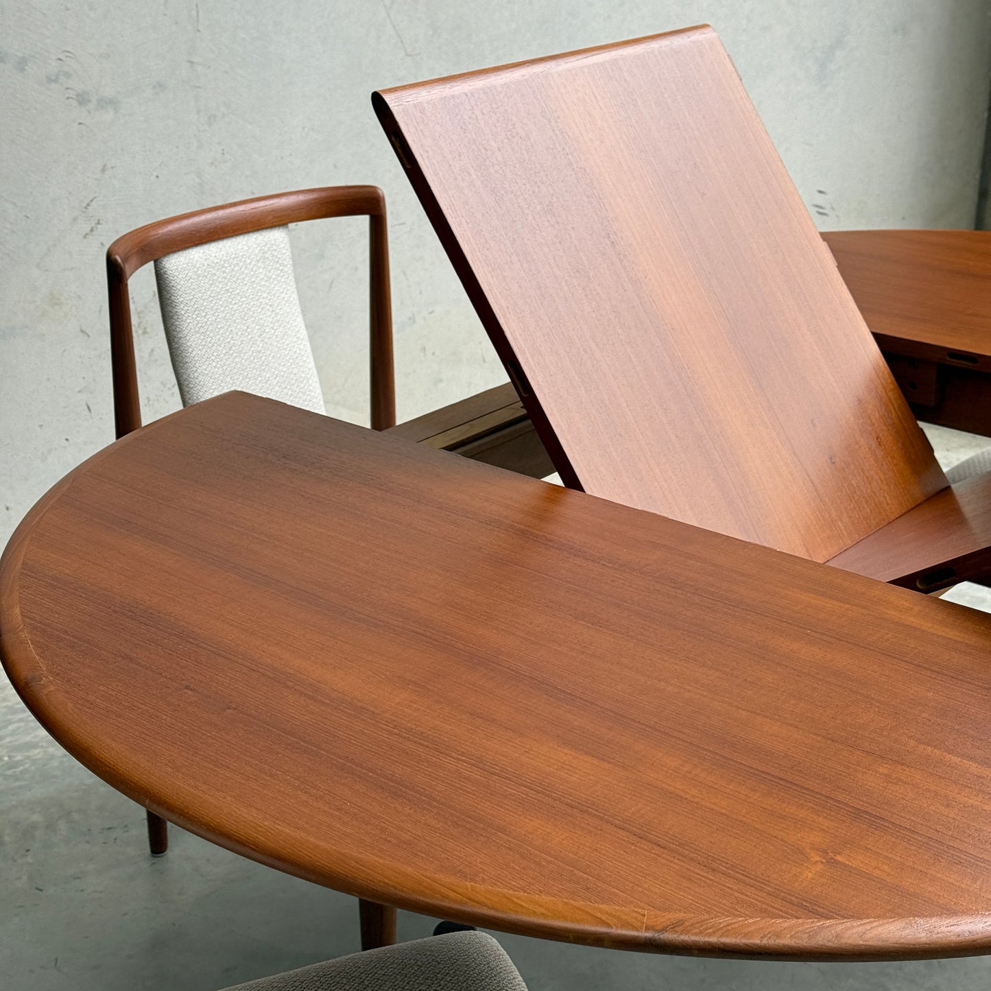 A Fully Restored Parker 90 Round Extension Butterfly Table (Rediscover) is shown with its central leaf extended, highlighting its versatile mid-century modern design. A chair with a curved wooden back and light fabric seat is partly visible beside it.