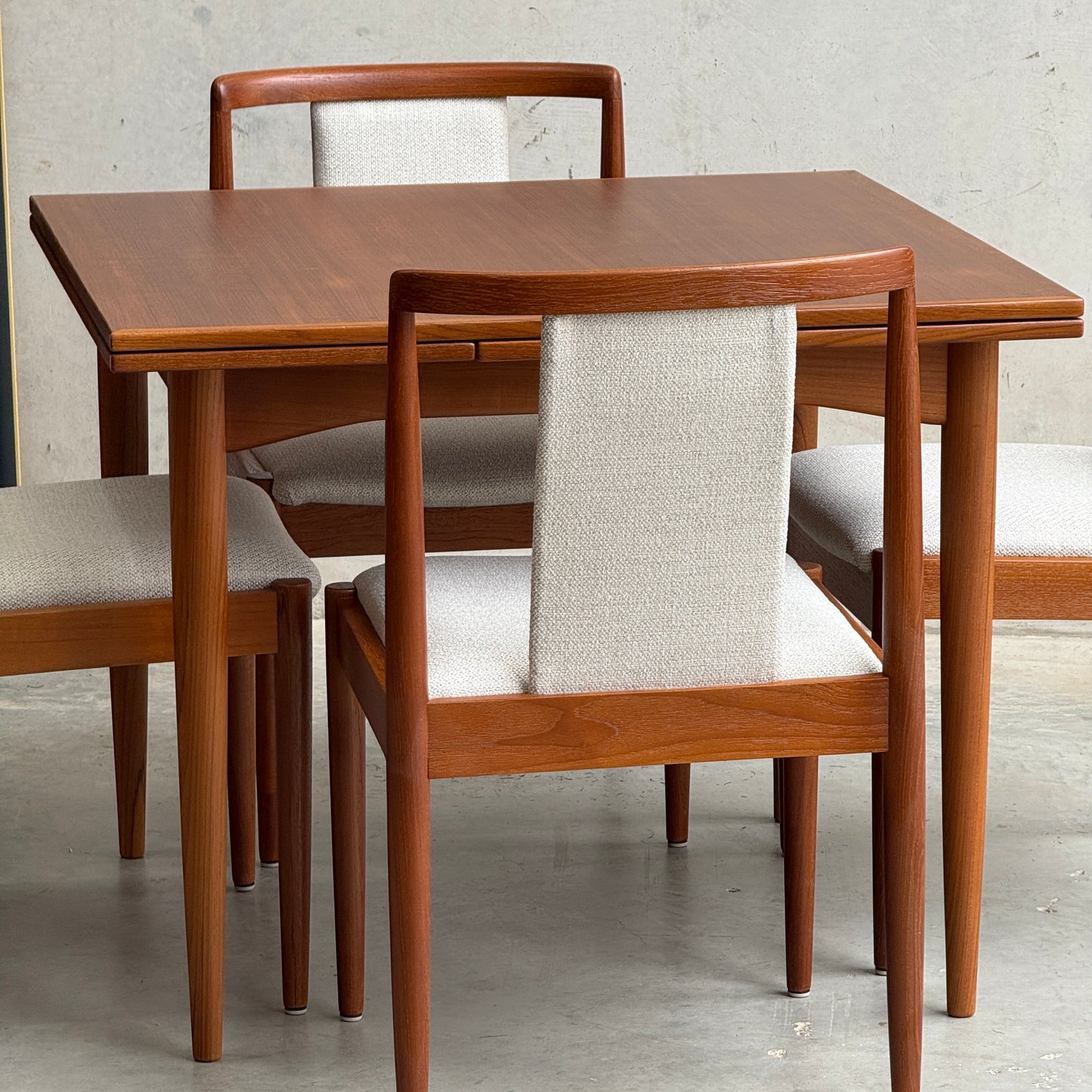 The Fully Restored Parker 140 Square Extension Table (Rediscover) is shown with four matching chairs featuring light upholstered seats and backs, set on a concrete floor against a plain light-colored wall.