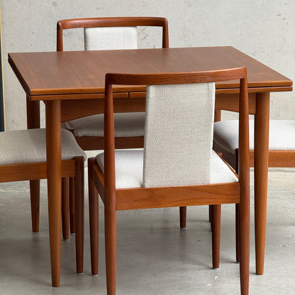 The Fully Restored Parker 140 Square Extension Table (Rediscover) is shown with four matching chairs featuring light upholstered seats and backs, set on a concrete floor against a plain light-colored wall.