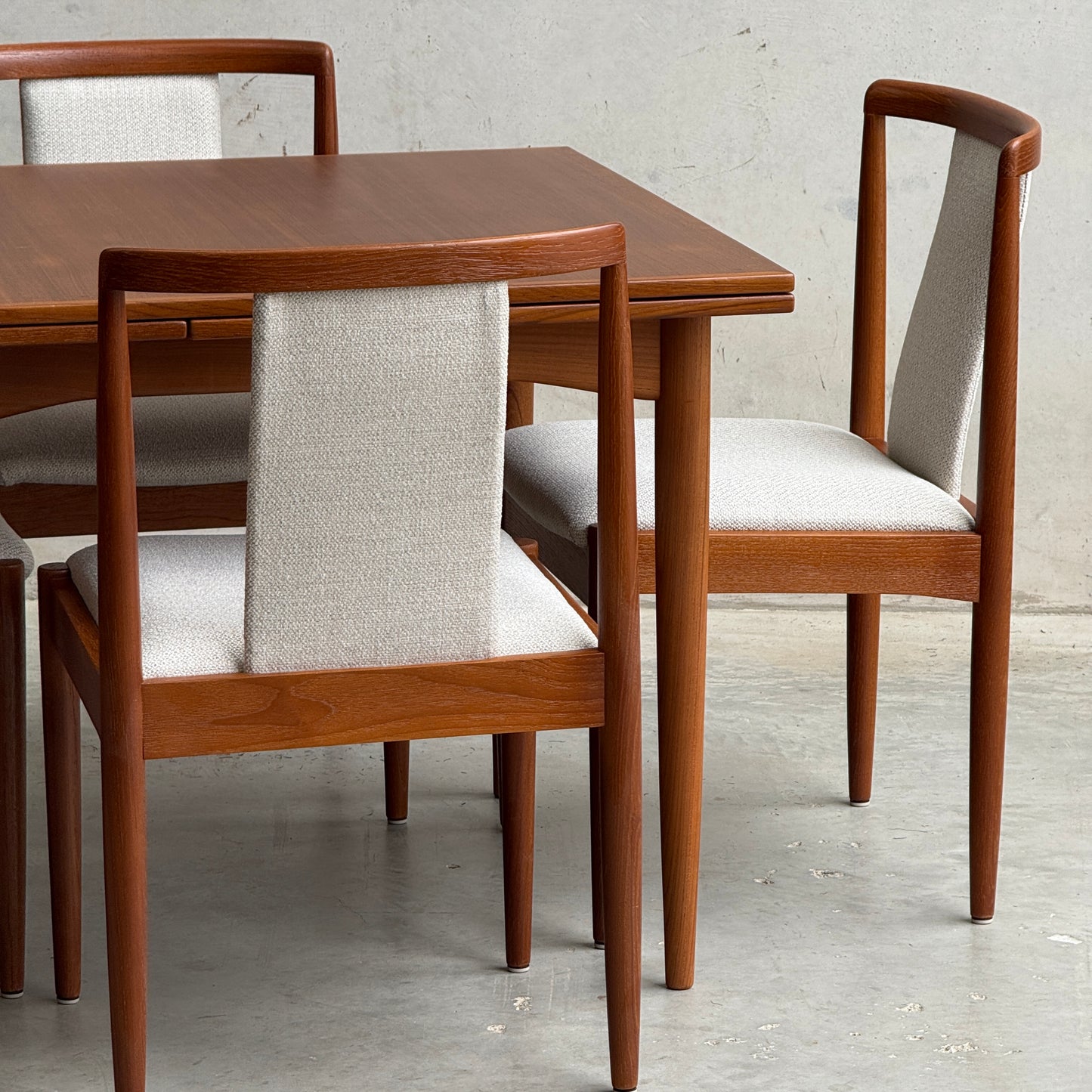 A close-up of the Fully Restored Parker 140 Square Extension Table (Rediscover) with matching chairs featuring light grey upholstered seats and backs, set against a plain, light-colored wall and floor.