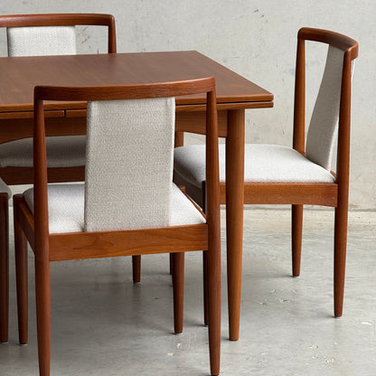 A close-up of the Fully Restored Parker 140 Square Extension Table (Rediscover) with matching chairs featuring light grey upholstered seats and backs, set against a plain, light-colored wall and floor.
