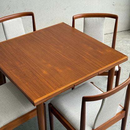 A Fully Restored Parker 140 Square Extension Table (Rediscover) with four matching chairs featuring curved wooden backs and light gray fabric seats, set on a concrete floor against a plain gray wall.