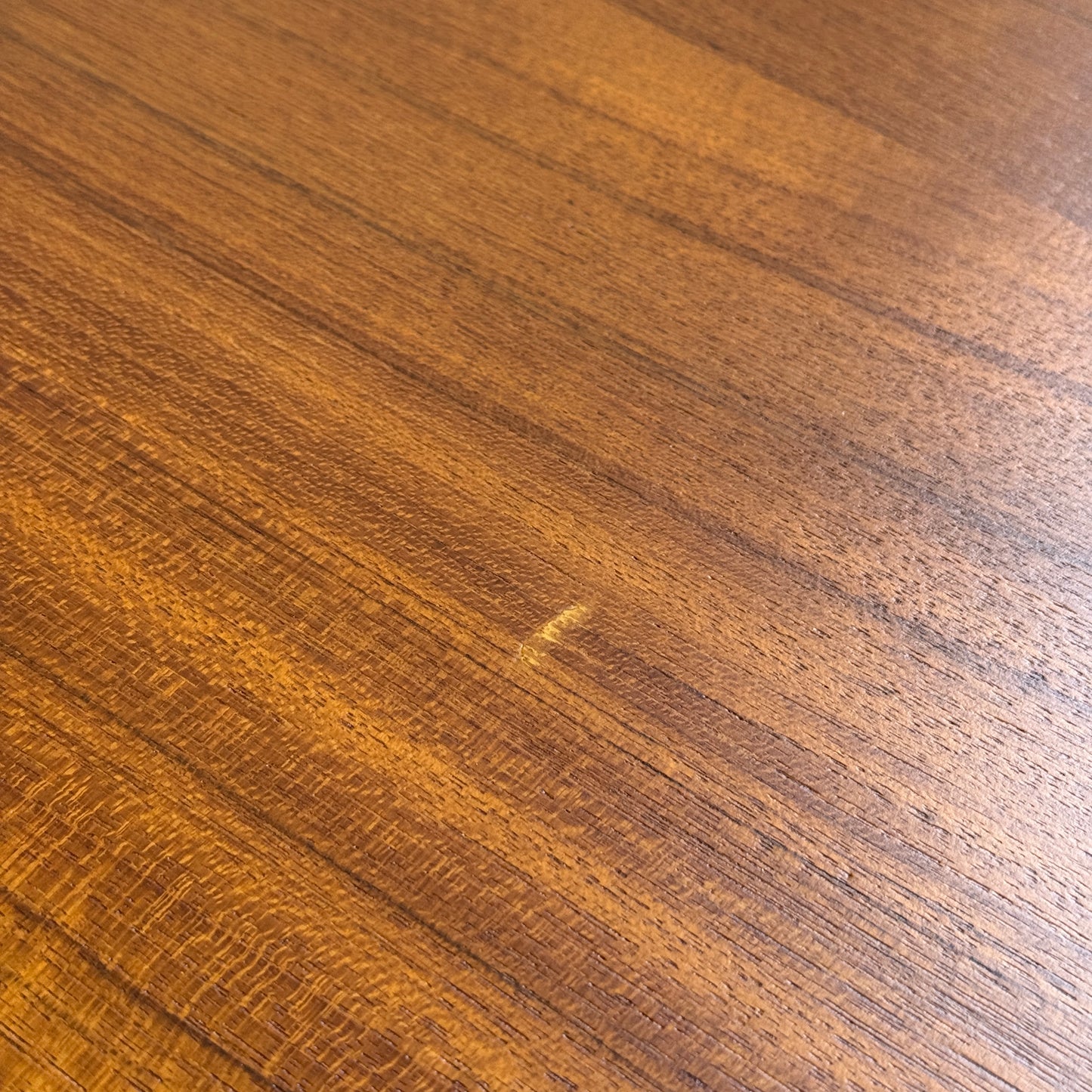 Close-up of the fully restored Parker 140 Square Extension Table (Rediscover), showcasing its warm brown teak surface with diagonal grain patterns and a light scratch mark in the center.