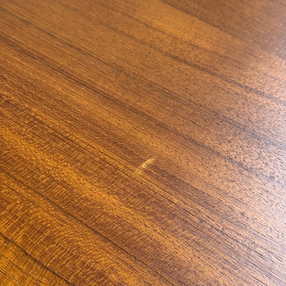Close-up of the fully restored Parker 140 Square Extension Table (Rediscover), showcasing its warm brown teak surface with diagonal grain patterns and a light scratch mark in the center.