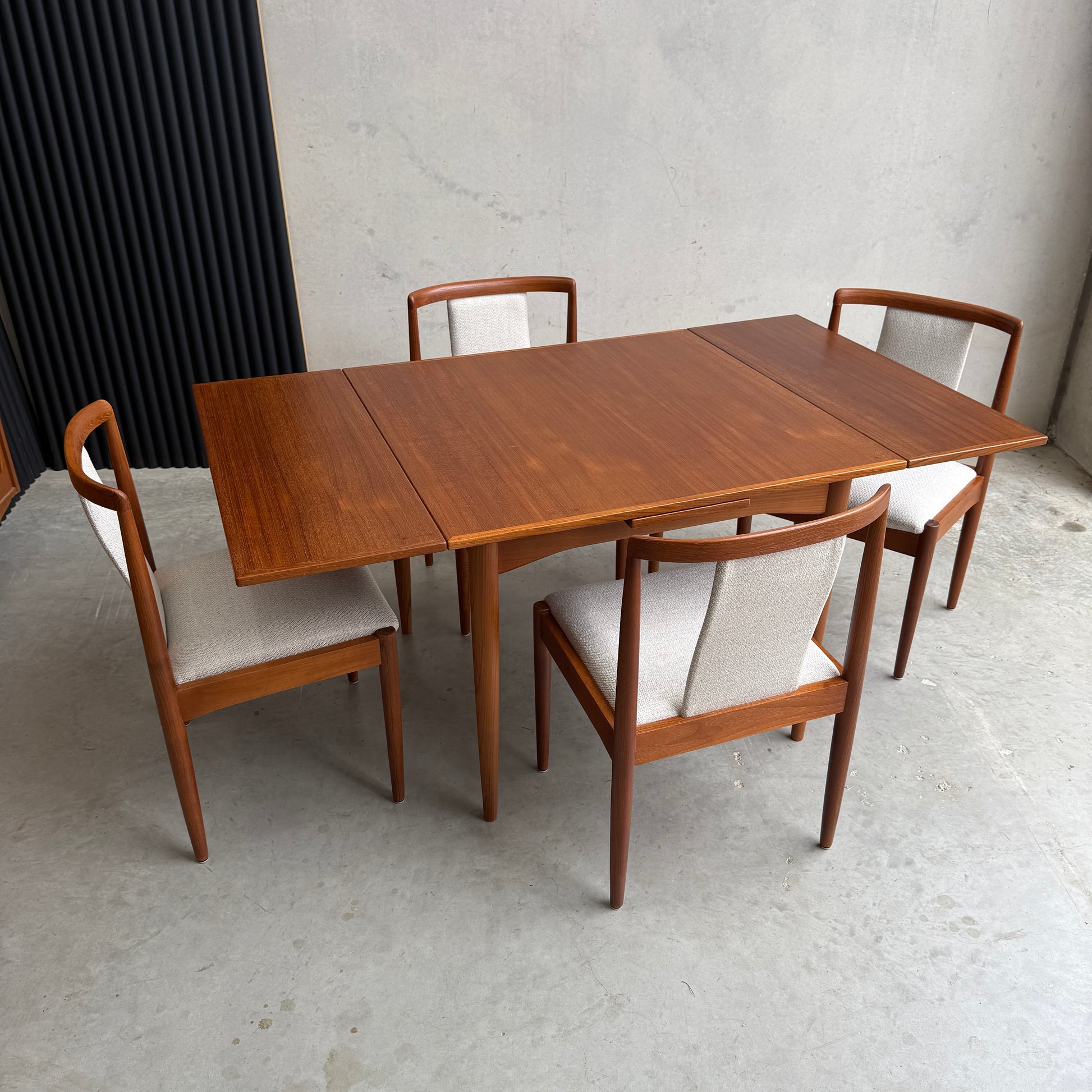 The Fully Restored Parker 140 Square Extension Table (Rediscover) is shown extended with two leaves and paired with four light-upholstered chairs, all arranged on a concrete floor against a plain wall.