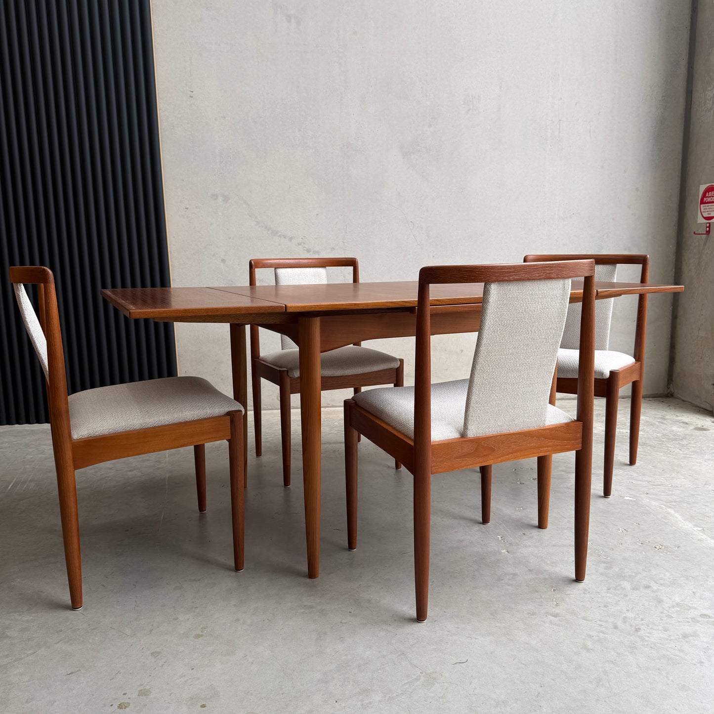 The Fully Restored Parker Dining Suite 5 Piece Square - Number 140 (Rediscover) includes a mid-century modern teak table and four chairs with light upholstery, ideal for a minimalist room with concrete walls and floor.
