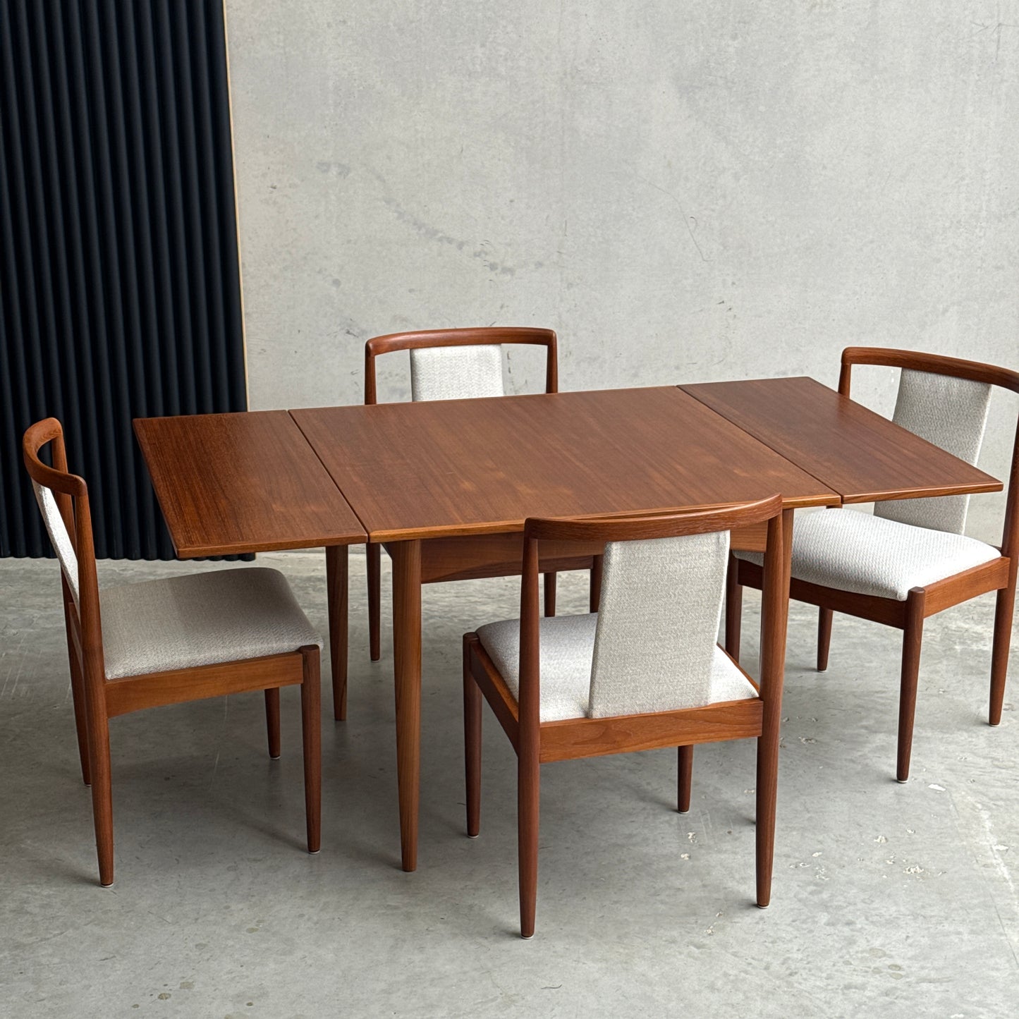 The Fully Restored Parker Dining Suite 5 Piece Square - Number 140 (Rediscover) features a mid-century teak table and four matching chairs with light upholstery, set on a concrete floor against a minimalist background.
