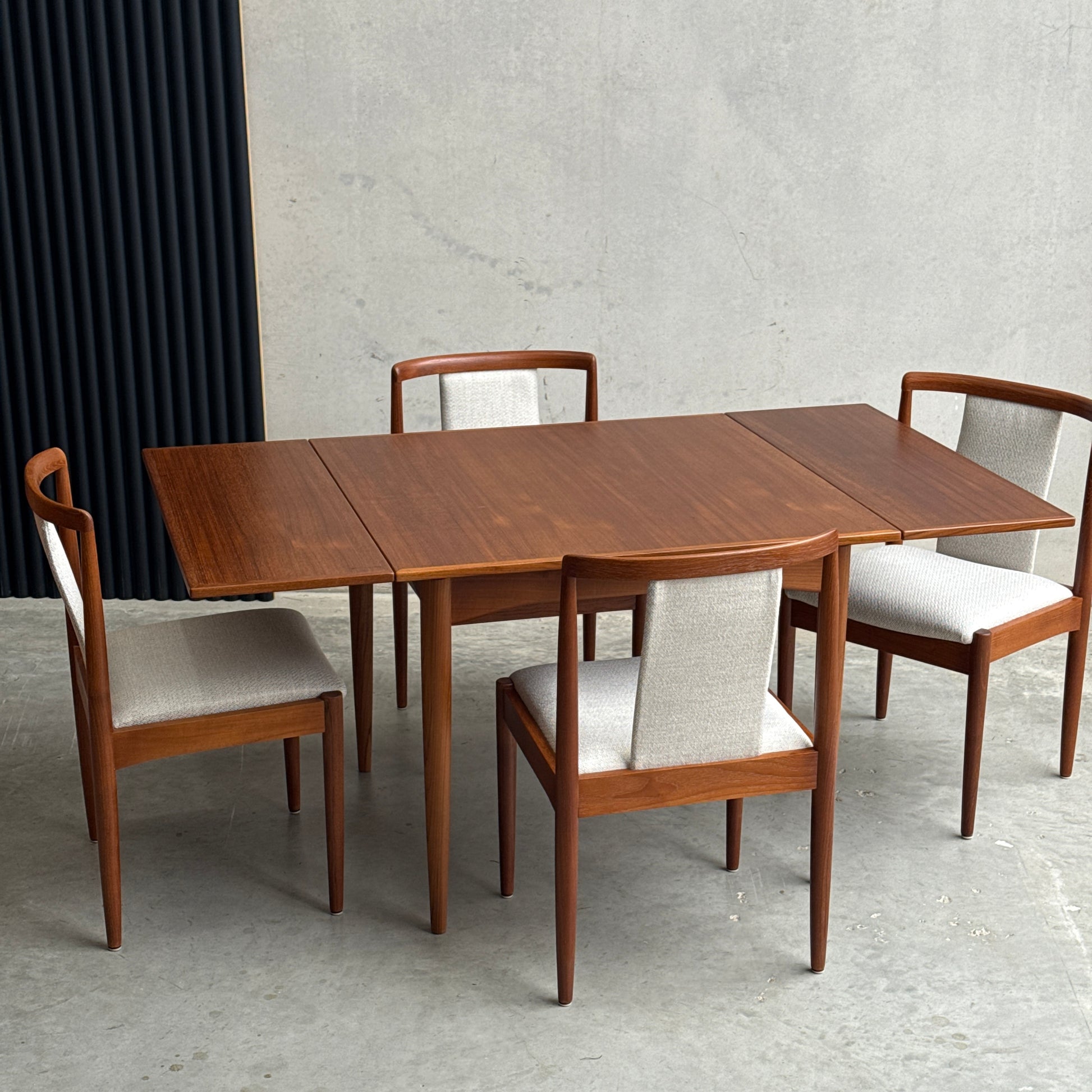 The Fully Restored Parker Dining Suite 5 Piece Square - Number 140 (Rediscover) features a mid-century teak table and four matching chairs with light upholstery, set on a concrete floor against a minimalist background.