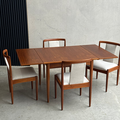 The Fully Restored Parker Dining Suite 5 Piece Square - Number 140 (Rediscover) features a mid-century teak table and four matching chairs with light upholstery, set on a concrete floor against a minimalist background.