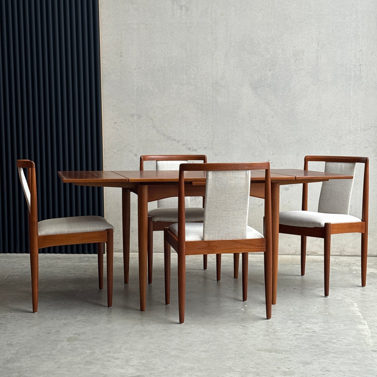 A mid-century modern dining set featuring a fully restored Parker 140 Square Extension Table (Rediscover) and four matching upholstered chairs, styled against a concrete wall and ribbed black panel.