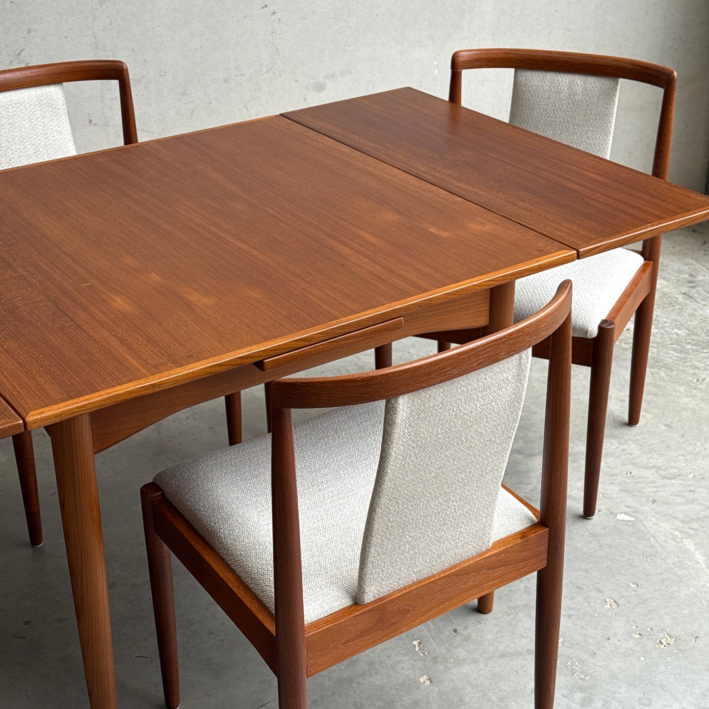 A Fully Restored Parker Dining Suite 5 Piece Square - Number 140 (Rediscover), featuring a mid-century modern teak table with extension leaf and three matching light-upholstered chairs, displayed on a concrete floor against a gray wall.