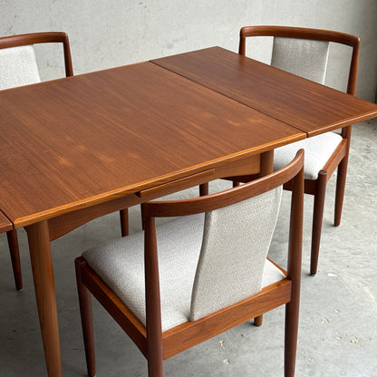 A Fully Restored Parker Dining Suite 5 Piece Square - Number 140 (Rediscover), featuring a mid-century modern teak table with extension leaf and three matching light-upholstered chairs, displayed on a concrete floor against a gray wall.