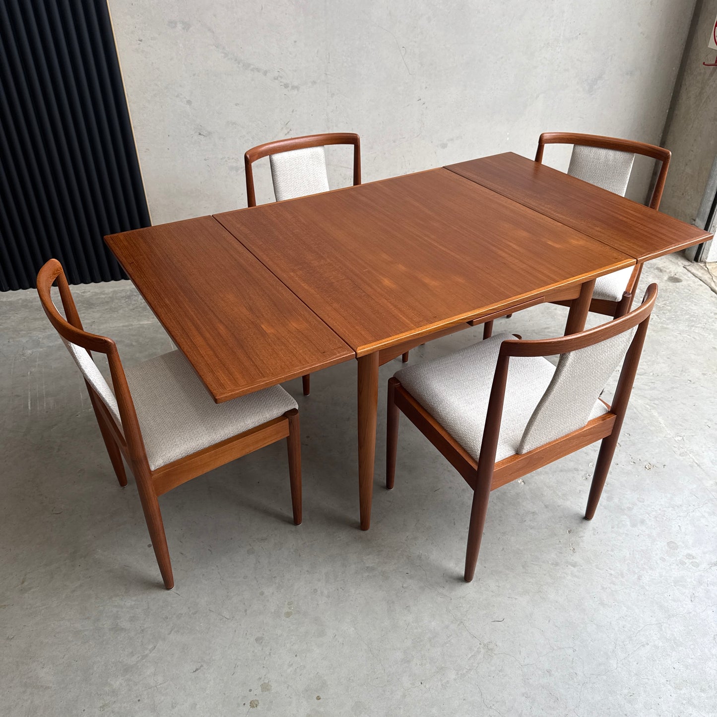 A Fully Restored Parker 140 Square Extension Table (Rediscover), with two leaves and four matching chairs with light upholstered seats, sits on a light concrete floor against a plain wall for a clean, timeless look.