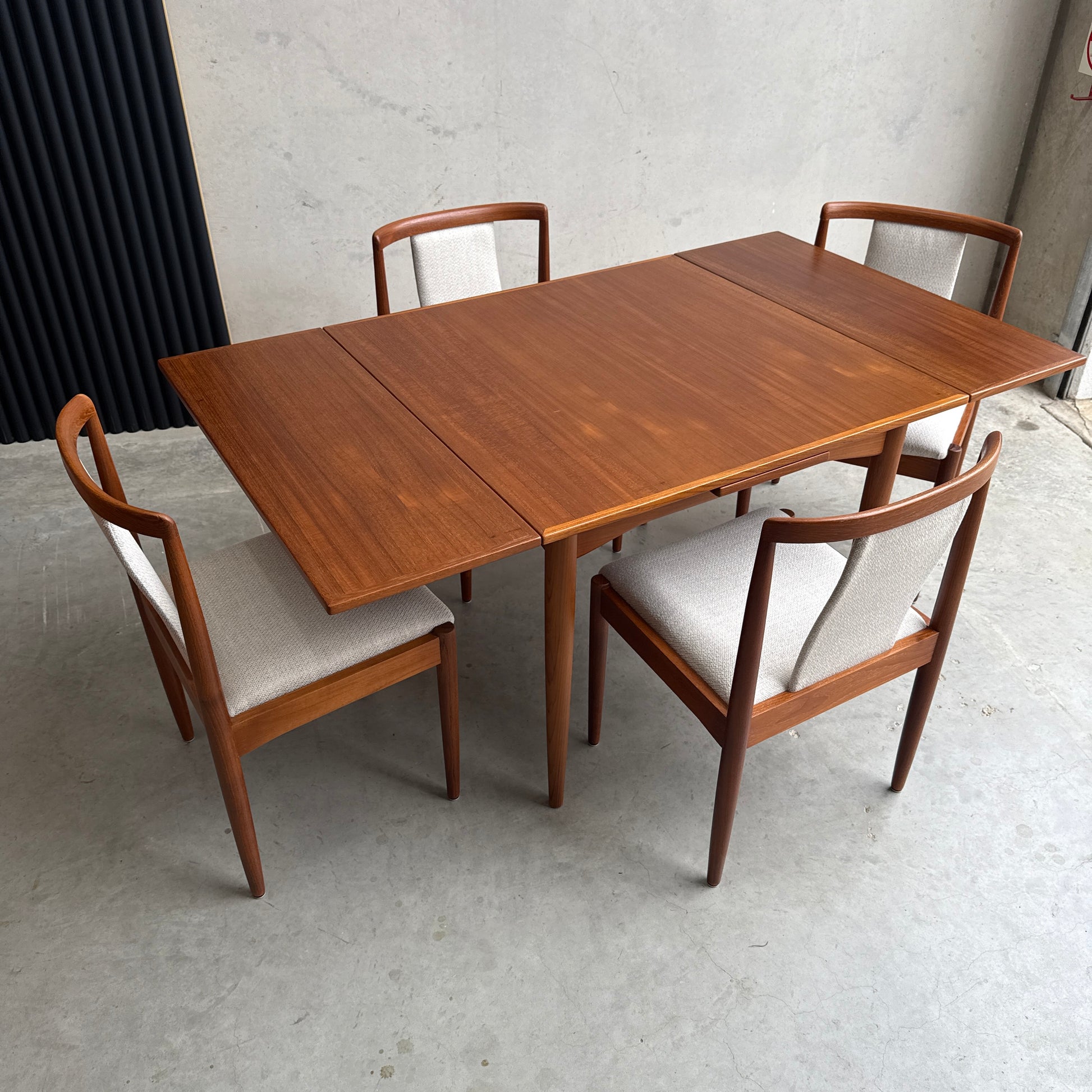 A Fully Restored Parker 140 Square Extension Table (Rediscover), with two leaves and four matching chairs with light upholstered seats, sits on a light concrete floor against a plain wall for a clean, timeless look.