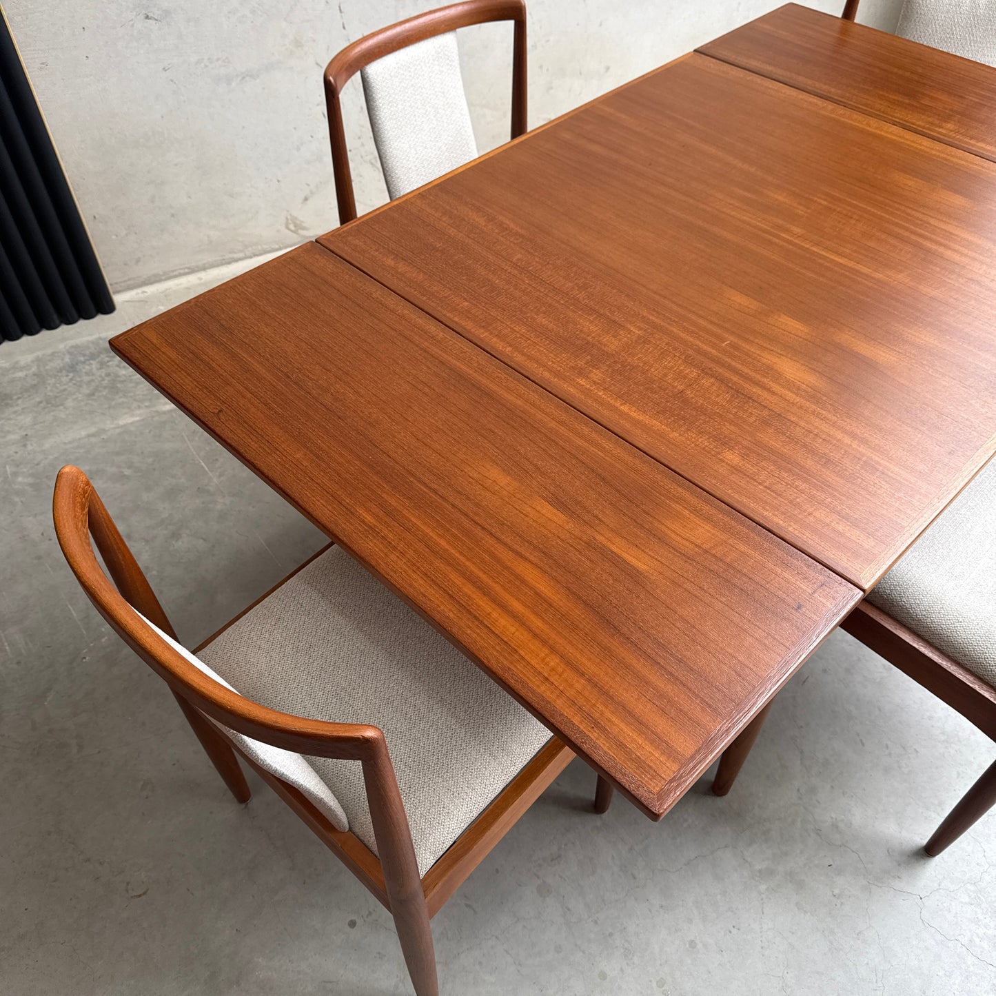 A fully restored Parker 140 Square Extension Table (Rediscover) with a smooth finish and two beige upholstered chairs sits on a polished concrete floor near a light-colored wall.