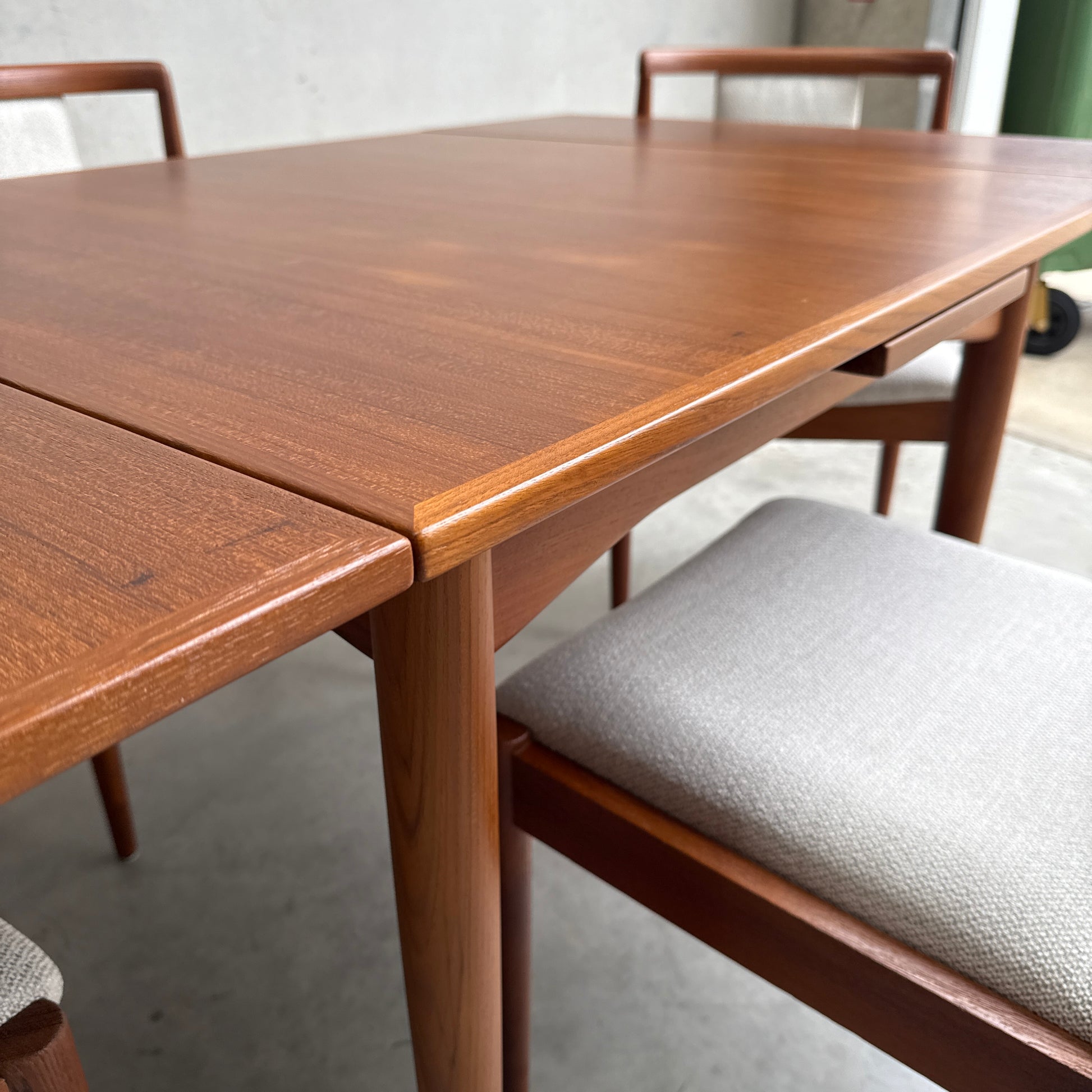 A close-up of a Fully Restored Parker 140 Square Extension Table (Rediscover) with matching chairs featuring light upholstery, shown on a concrete floor in a modern indoor setting.
