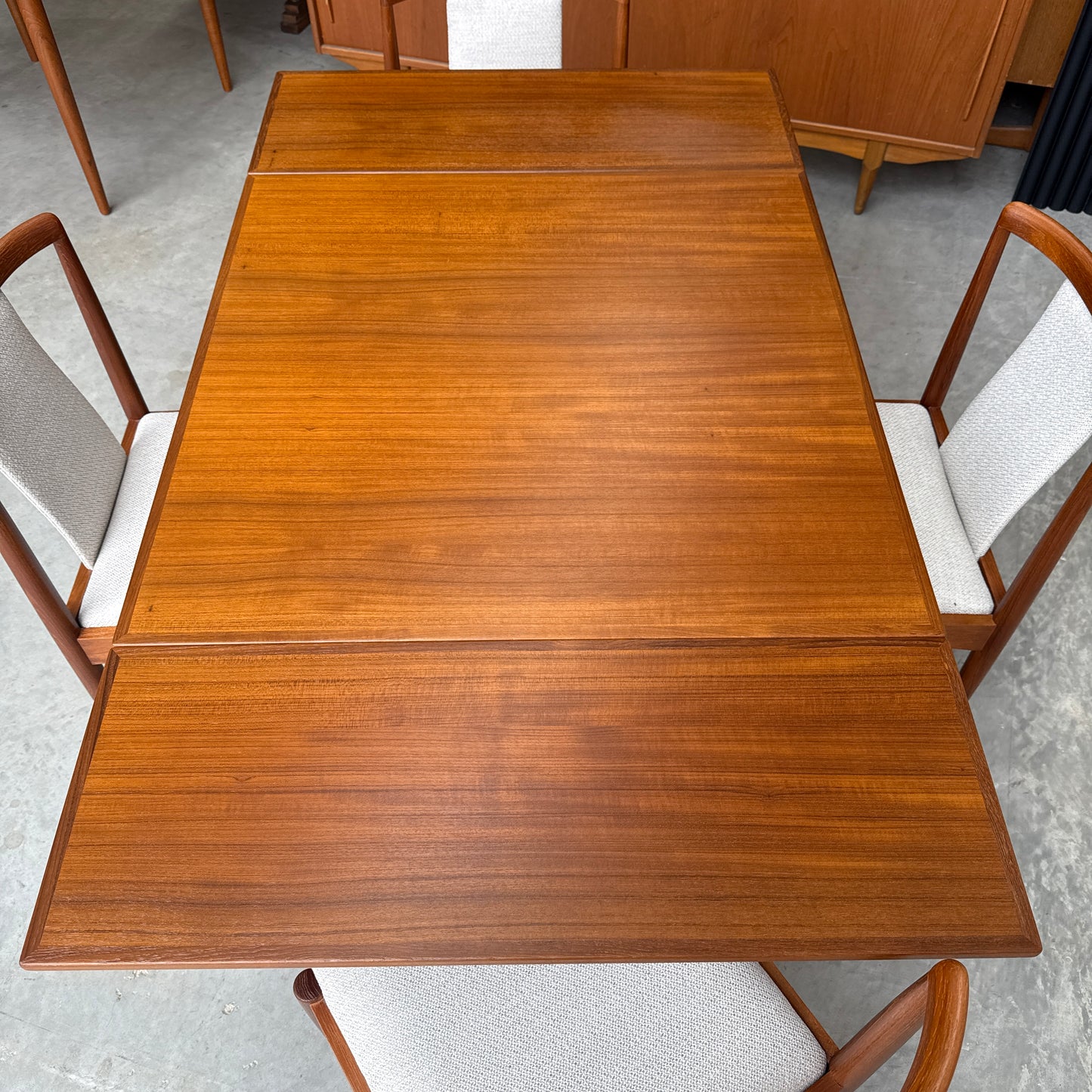 A Fully Restored Parker 140 Square Extension Table (Rediscover) with a warm finish is paired with four light-upholstered, wooden-framed chairs and set on a concrete floor.