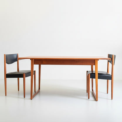 The Rare Gerald Easden Rectangular Extension Dining Table (Rediscover) is paired with two black-seated chairs, all set against a plain white background for a minimalist mid-century modern look.