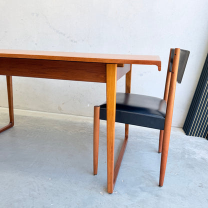 The Rare Gerald Easden Rectangular Extension Dining Table (Rediscover) stands on a gray concrete floor, its warm Australian teak and mid-century modern design highlighted by a matching chair with a black seat and backrest against a light wall.