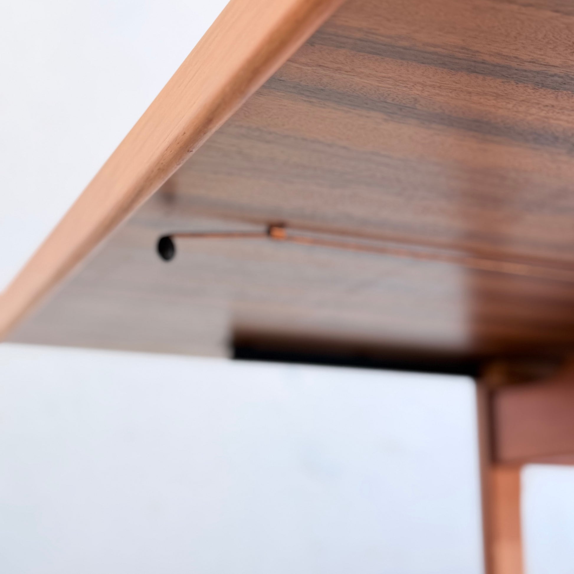 Close-up view of the underside of the Rare Gerald Easden Rectangular Extension Dining Table (Rediscover), highlighting its edge, thin metal rod, and wire against a plain white background. Focus is on its mid-century modern hardware.
