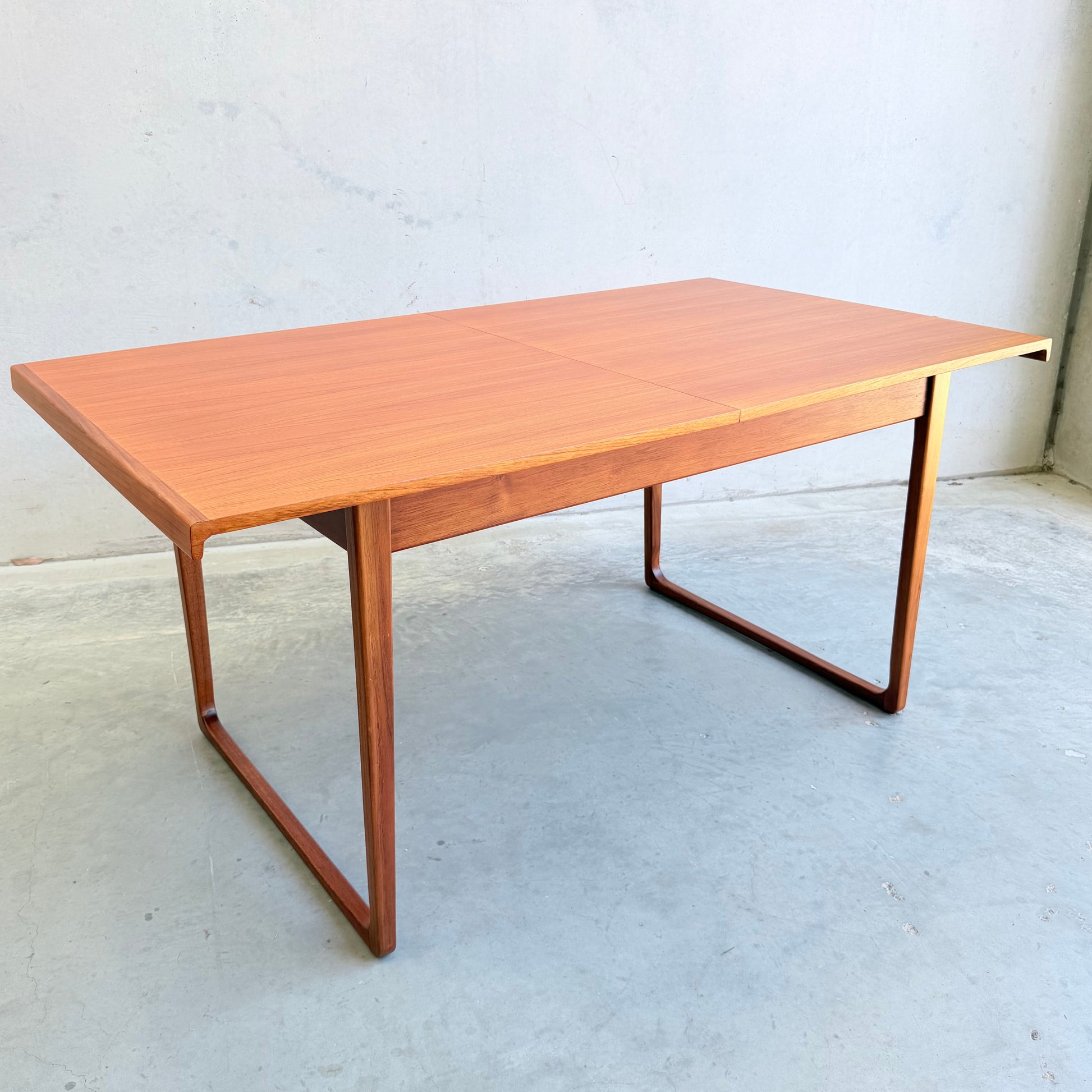 The Rare Gerald Easden Rectangular Extension Dining Table (Rediscover) features clean mid-century modern lines and a light brown finish, styled after Australian teak, and stands on a concrete floor against a plain light wall.