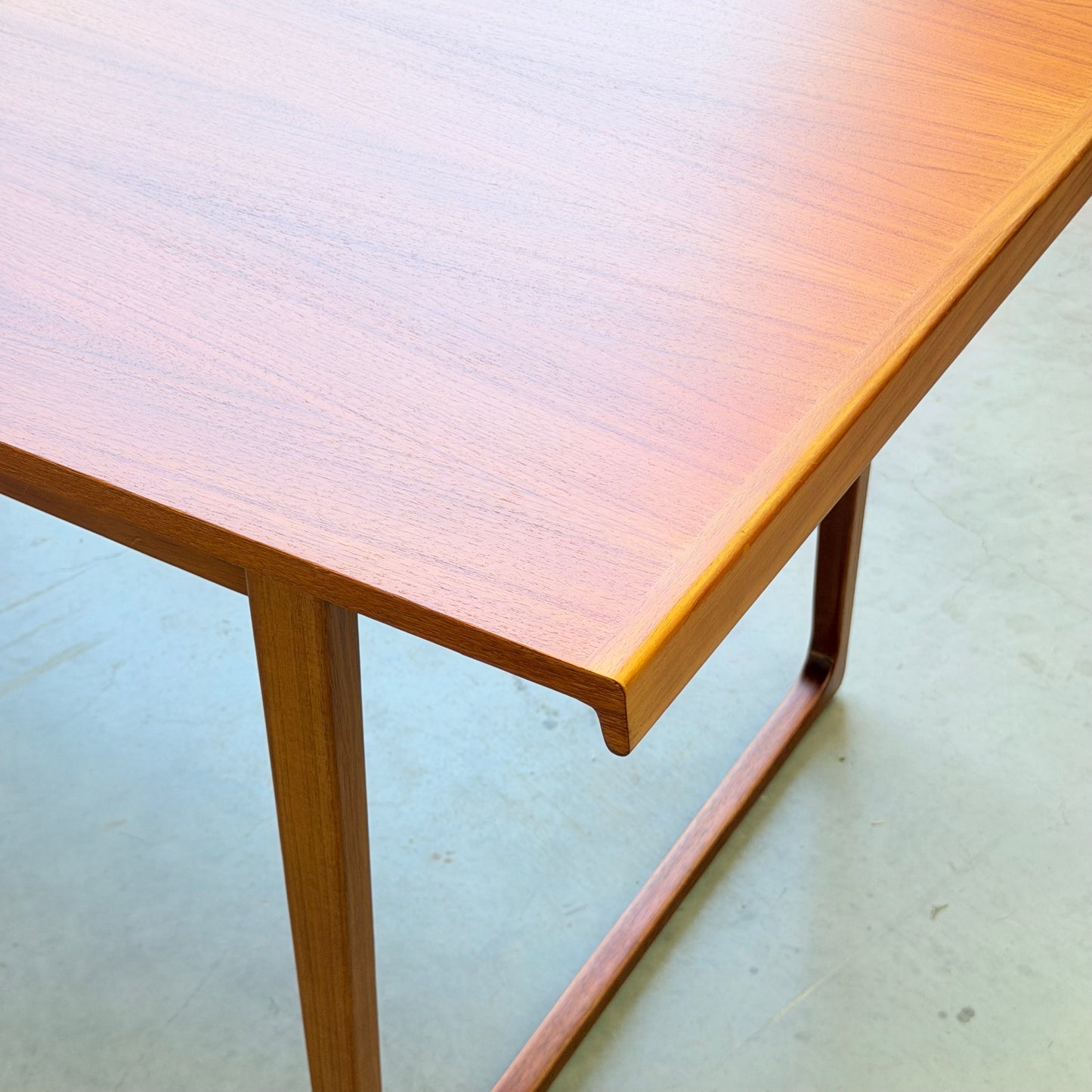 A close-up of the Rare Gerald Easden Rectangular Extension Dining Table (Rediscover) featuring angled legs and a smooth, polished surface, set on a light gray floor.