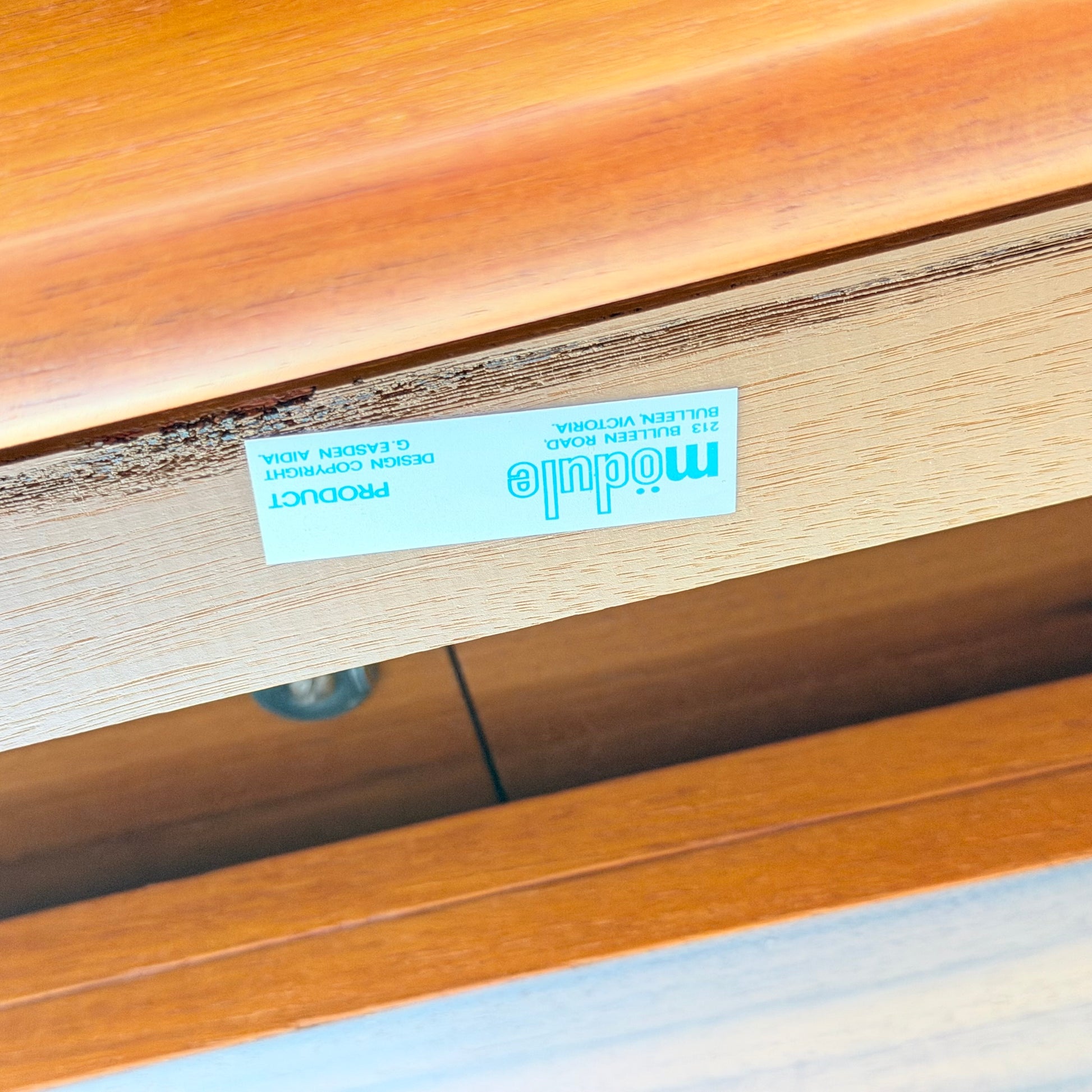 A close-up of a wooden drawer, likely from the Rare Gerald Easden Rectangular Extension Dining Table (Rediscover), shows an upside-down blue and white label reading module, 213 Bullenden Road, Bulli NSW, with partial copyright info inside.