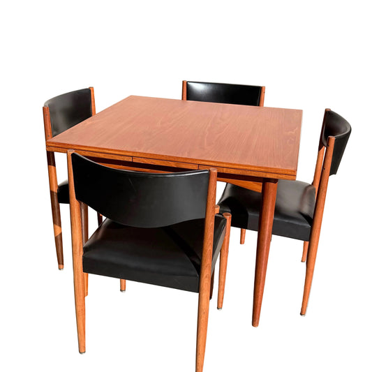 The Vintage Parker Dining Suite 5 Piece Square - Number 140 features a square wooden table and four chairs with black seats and backs, set against a light wall on concrete flooring. Sunlit shadows highlight its Scandinavian-inspired Australian design.