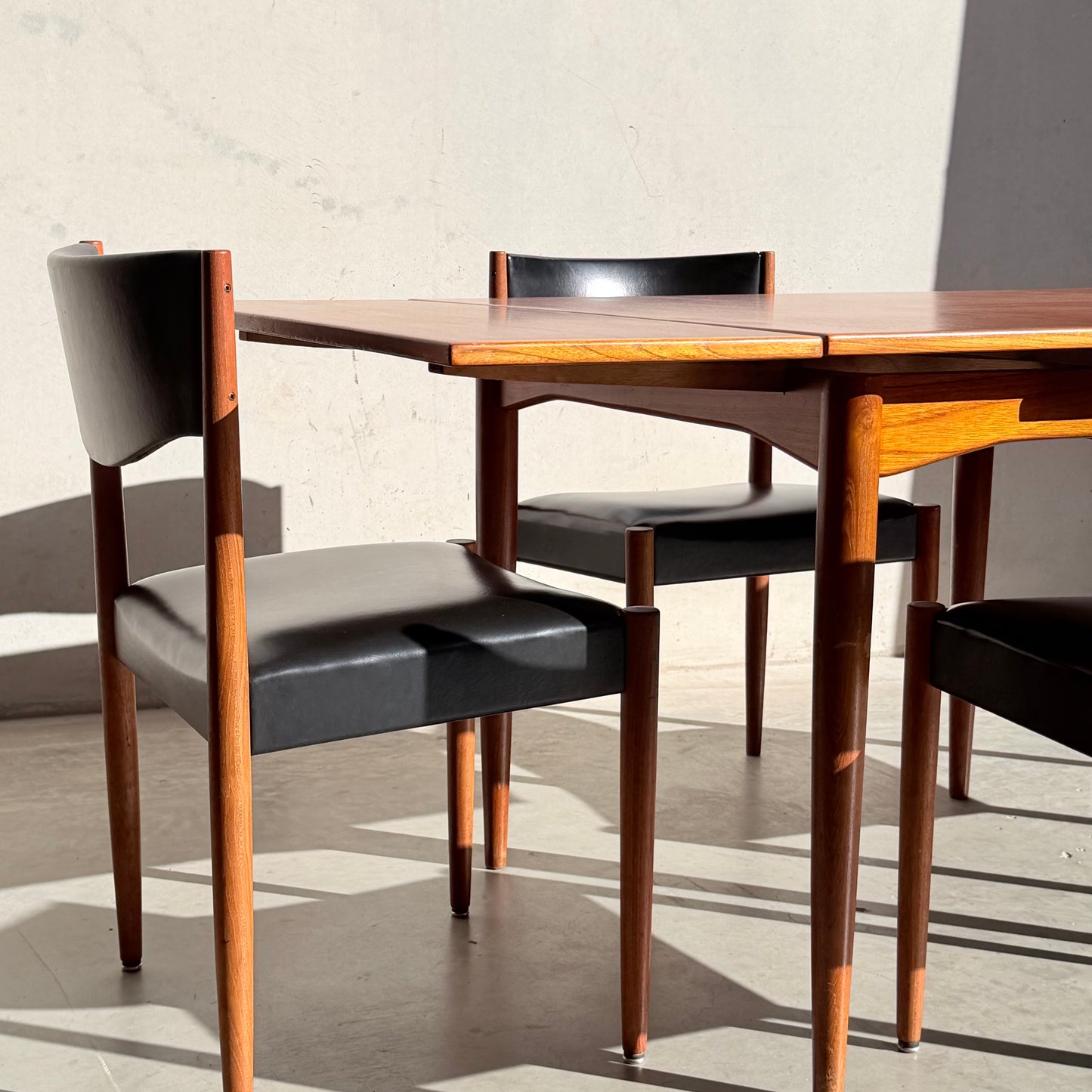 Two wooden chairs with black seats and backs from the Vintage Parker Dining Suite 5 Piece Square - Number 140 sit next to a matching table. Sunlight highlights the mid-century, Scandinavian-inspired Australian design.