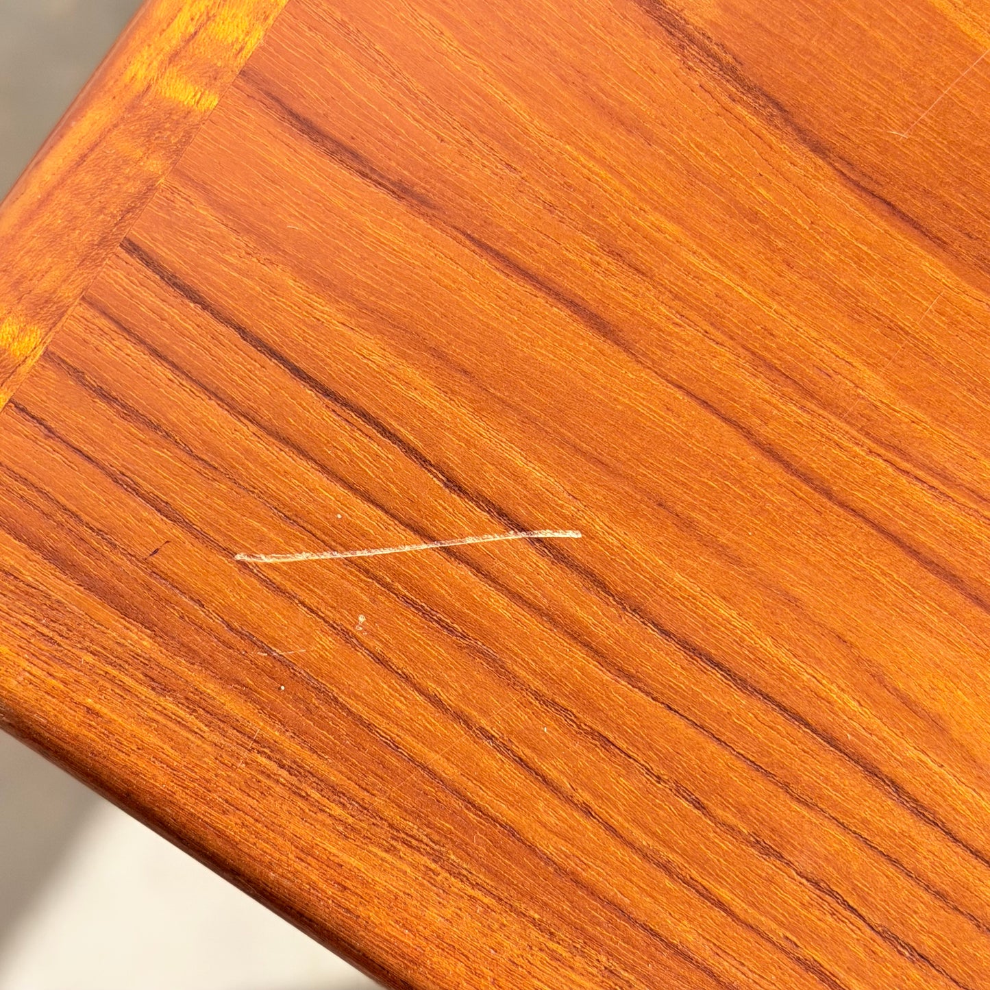 A close-up of the Vintage Parker Dining Suite 5 Piece Square - Number 140 shows a polished wood surface with a light-colored scratch running diagonally near the corner along the grain.