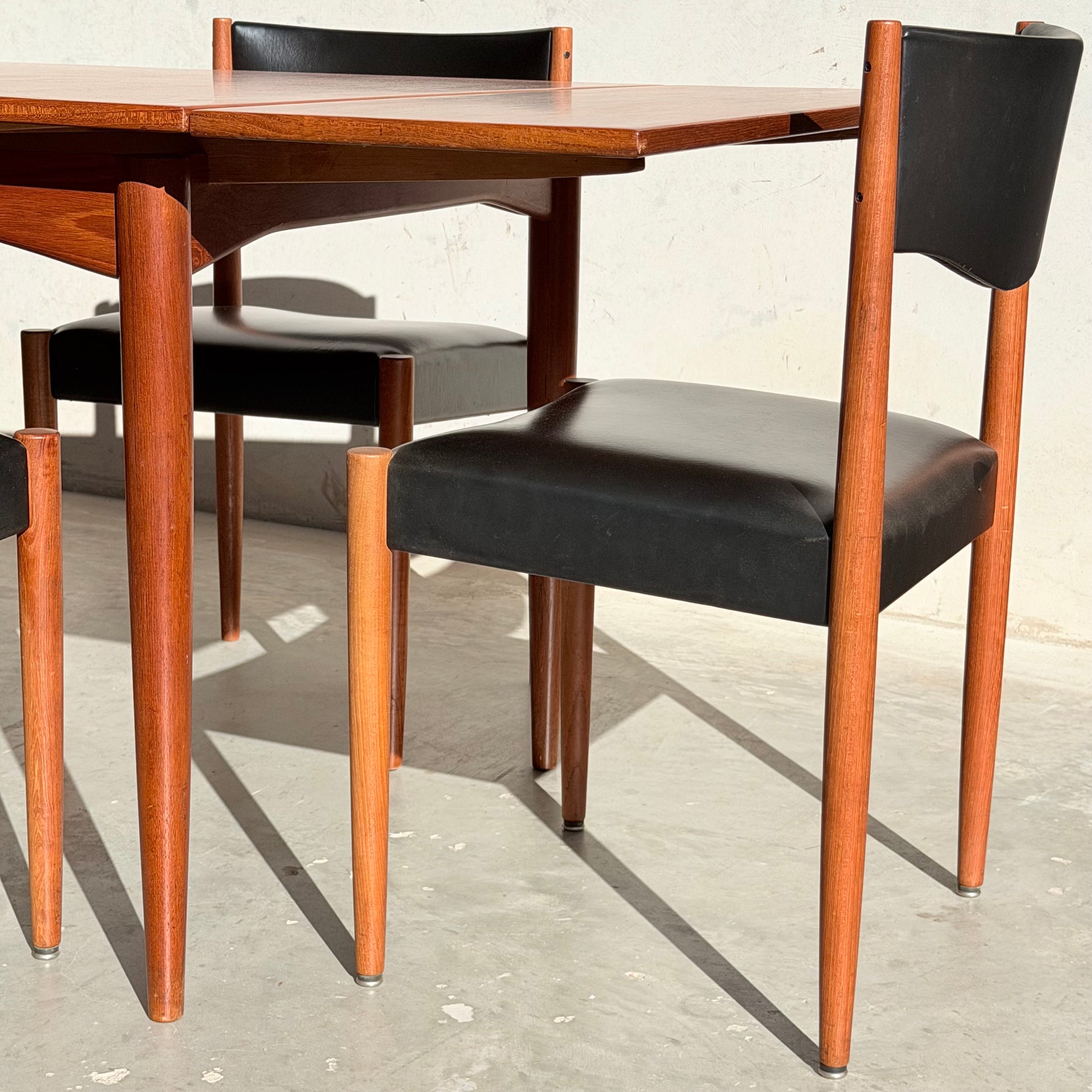 The Vintage Parker Dining Suite 5 Piece Square - Number 140 (Refine) features wooden chairs with black seats and backs beside a matching table. Sunlight casts sharp shadows, emphasizing its minimalist, Scandinavian-inspired Australian style.