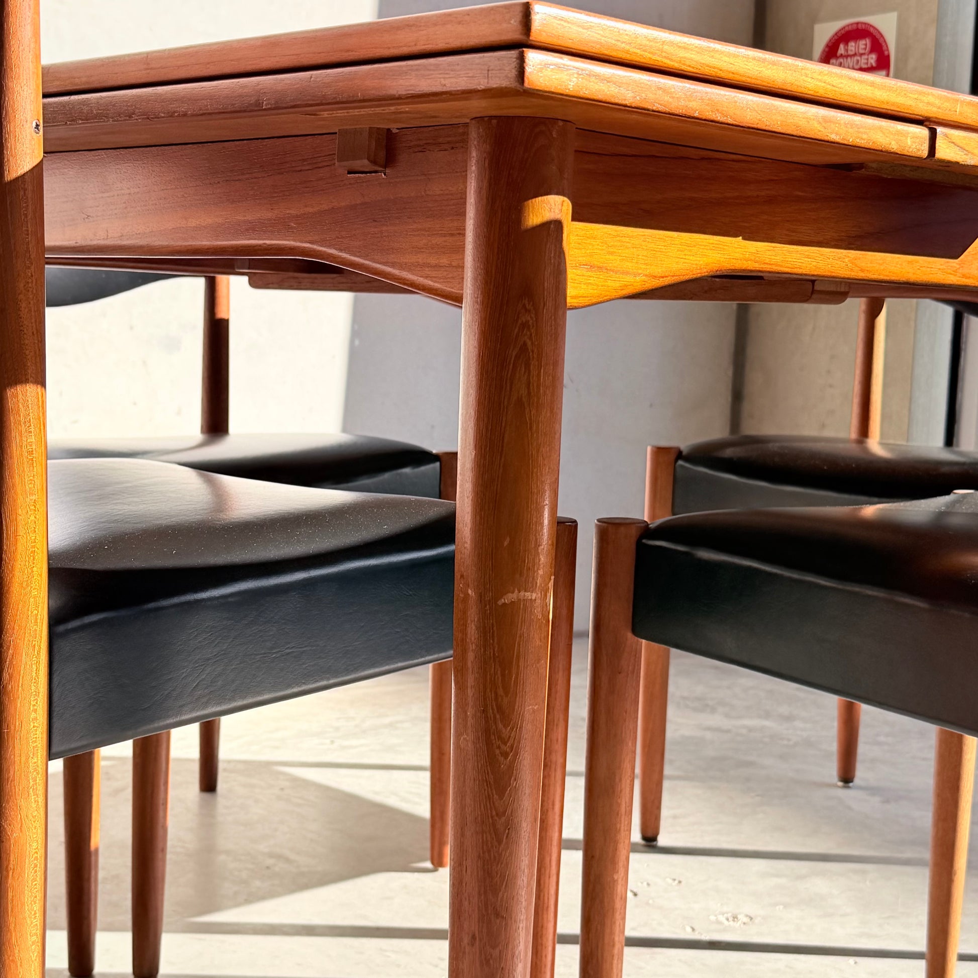 The Vintage Parker Dining Suite 5 Piece Square - Number 140 features four black-seated chairs arranged around a matching table, with sunlight highlighting the warm wood grain in this Scandinavian-inspired Australian design.