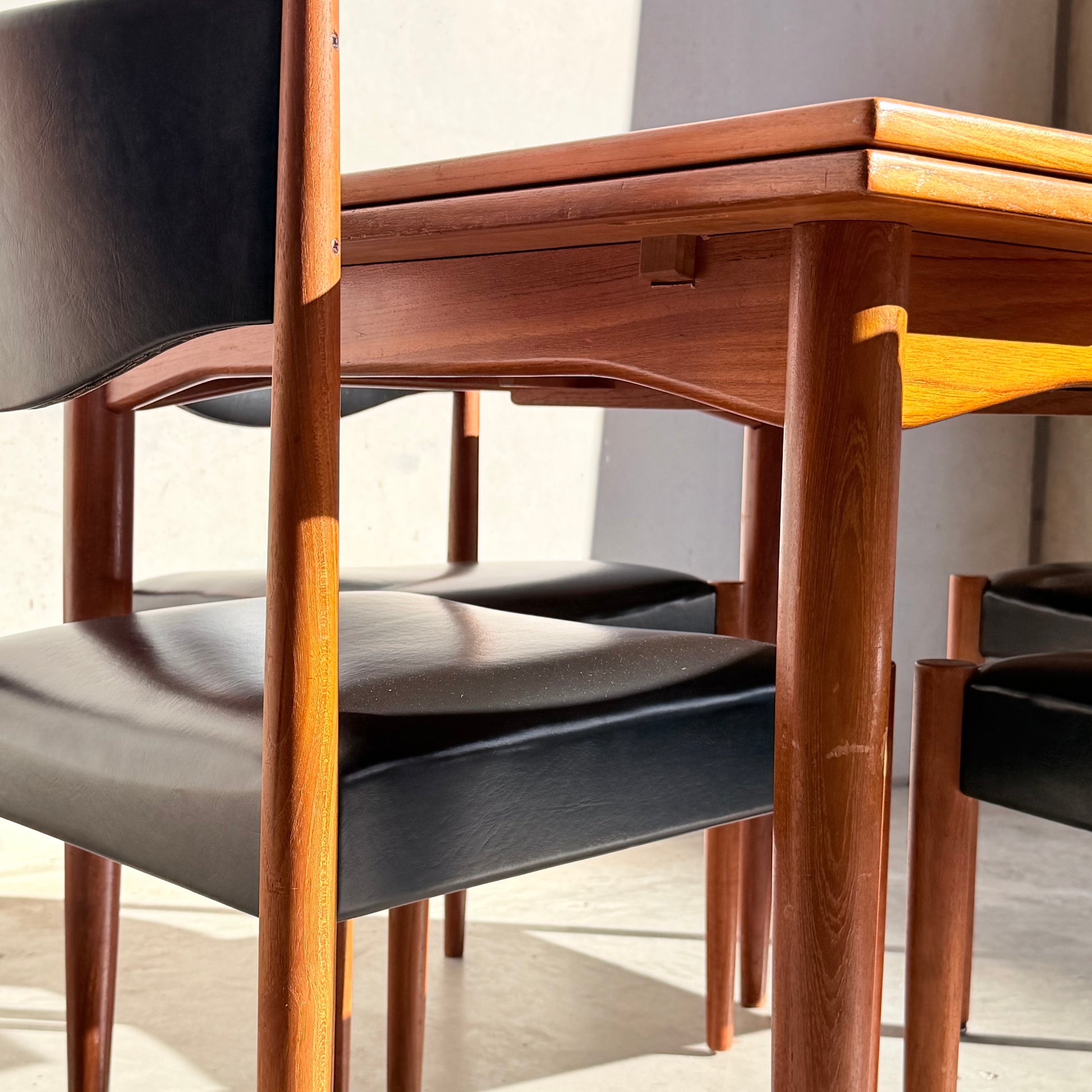 Close-up of the Vintage Parker Dining Suite 5 Piece Square - Number 140, featuring curved-leg chairs with black seat cushions. Sunlight highlights the wood grain, creating a warm and inviting mid-century vintage ambiance.