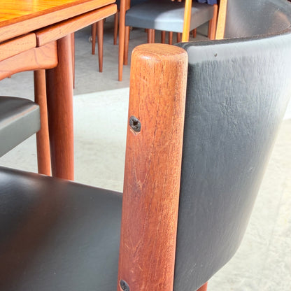 Close-up of a Vintage Parker Dining Suite 5 Piece Square - Number 140, featuring wooden and black leather chairs around a matching table. Several similar mid-century style chairs are arranged on a light-colored floor.