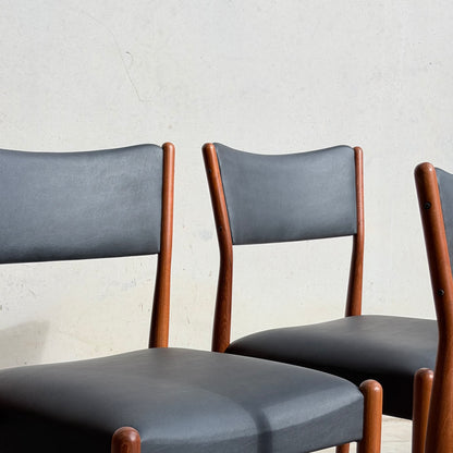 Two Parker Number 97 Dining Chairs Set of 4 – Licorice Vinyl (Rediscover) with black upholstered seats and backs sit side by side against a light wall, sunlight casting soft shadows on both chairs and the wall.